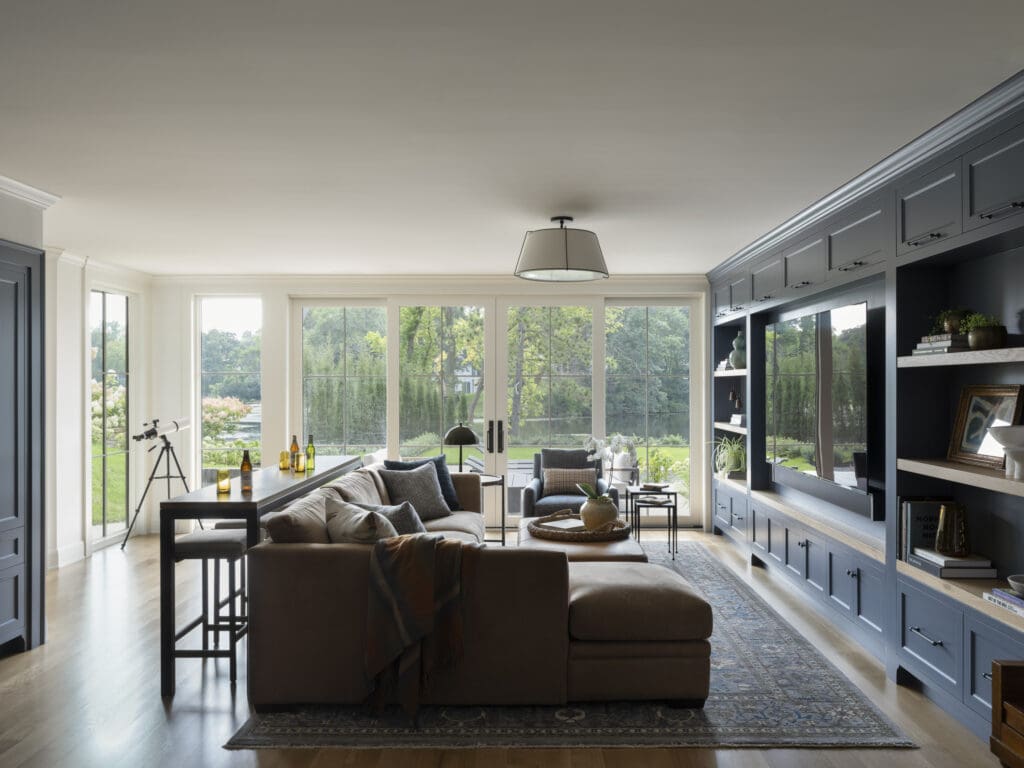 Bright modern living room with blue-gray built-in cabinets along the right wall and large windows.