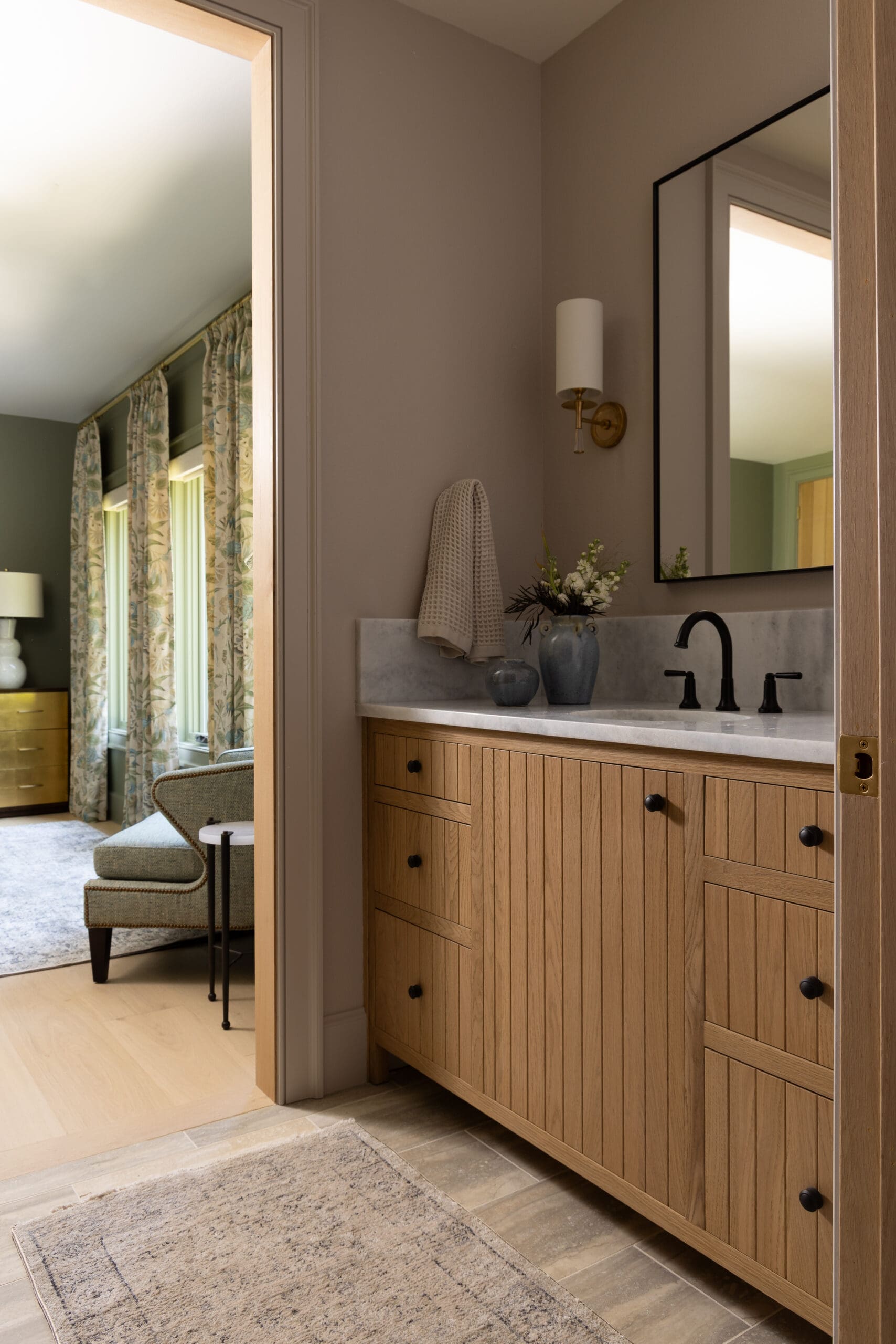 Wood vanity with marble countertop and black faucet in a bathroom; mirror on the wall and a towel hanging nearby