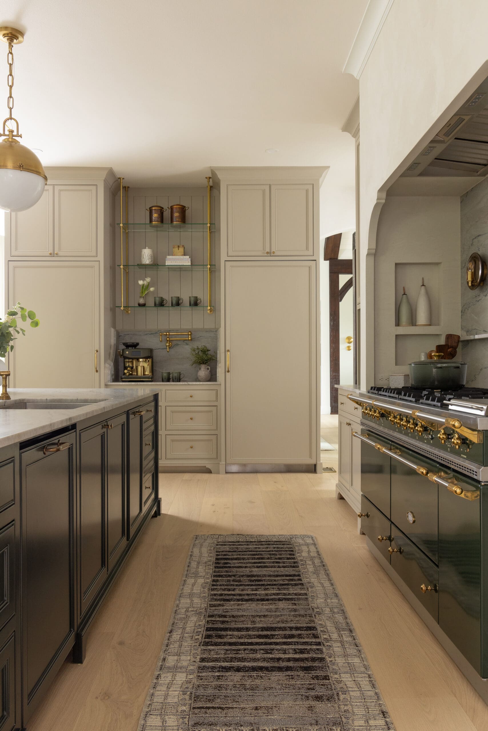 Luxurious kitchen with cream cabinets, glass open shelf, and gold hardware surrounding a marble countertop island