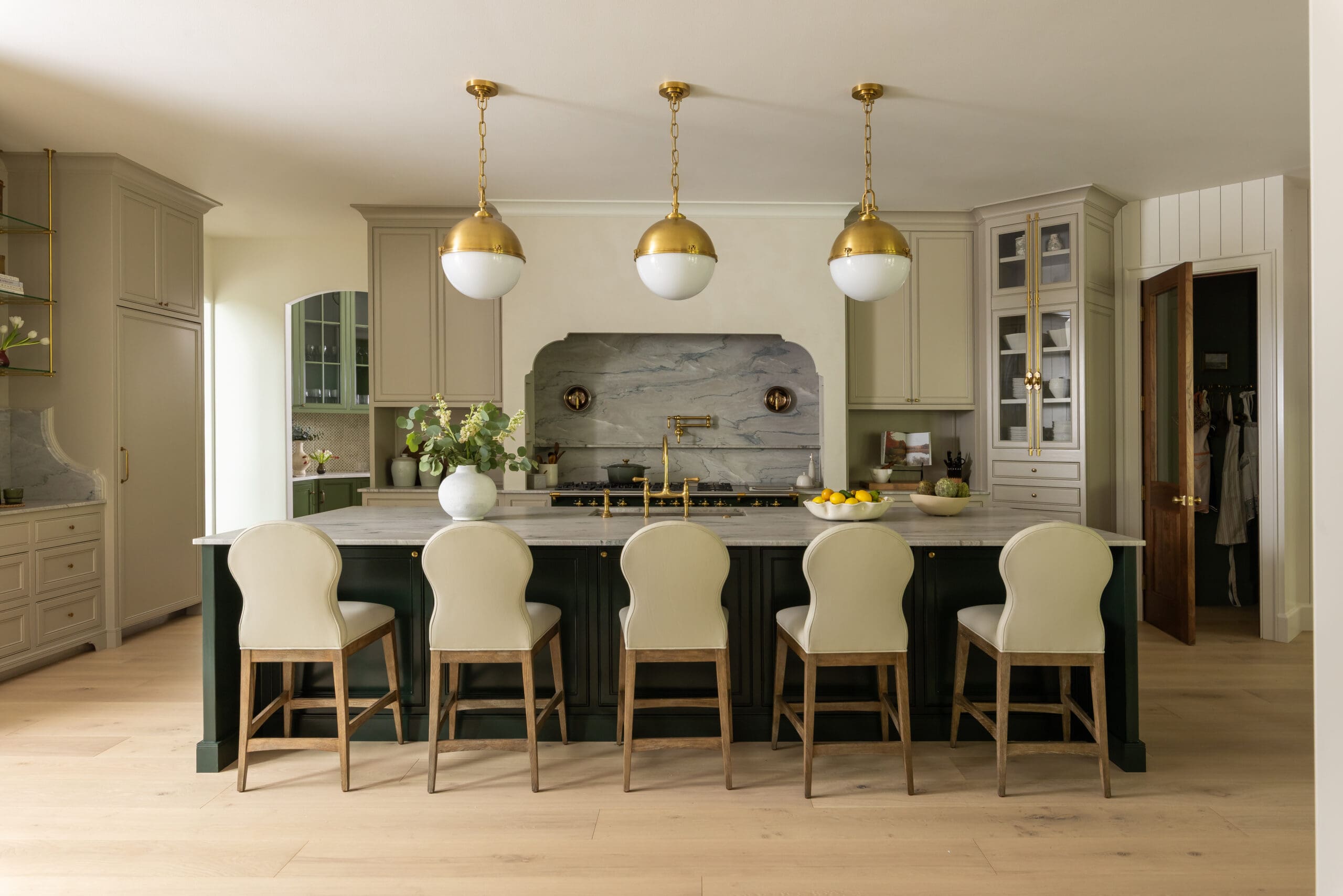 Elegant kitchen with a long marble island, cream cabinets, and three gold pendant lights overhead, plus cream stools along the island.
