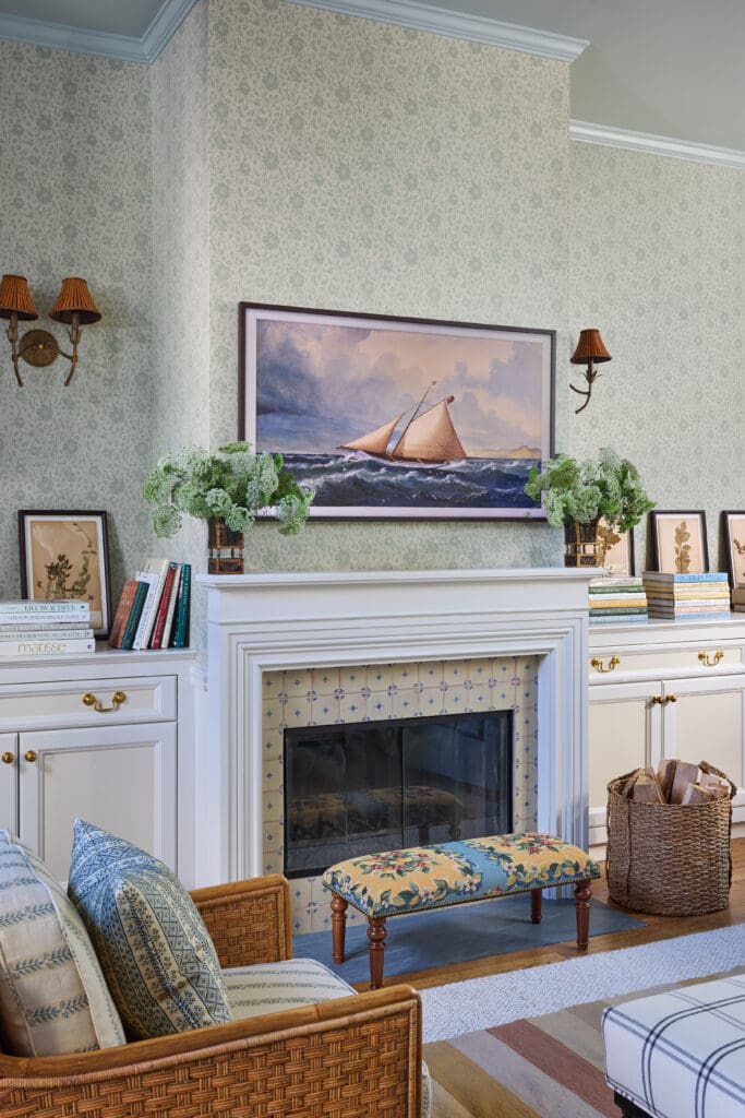Living room scene with a sailboat painting above a white mantel and green damask wallpaper, flanked by wall lamps and plants on shelves.