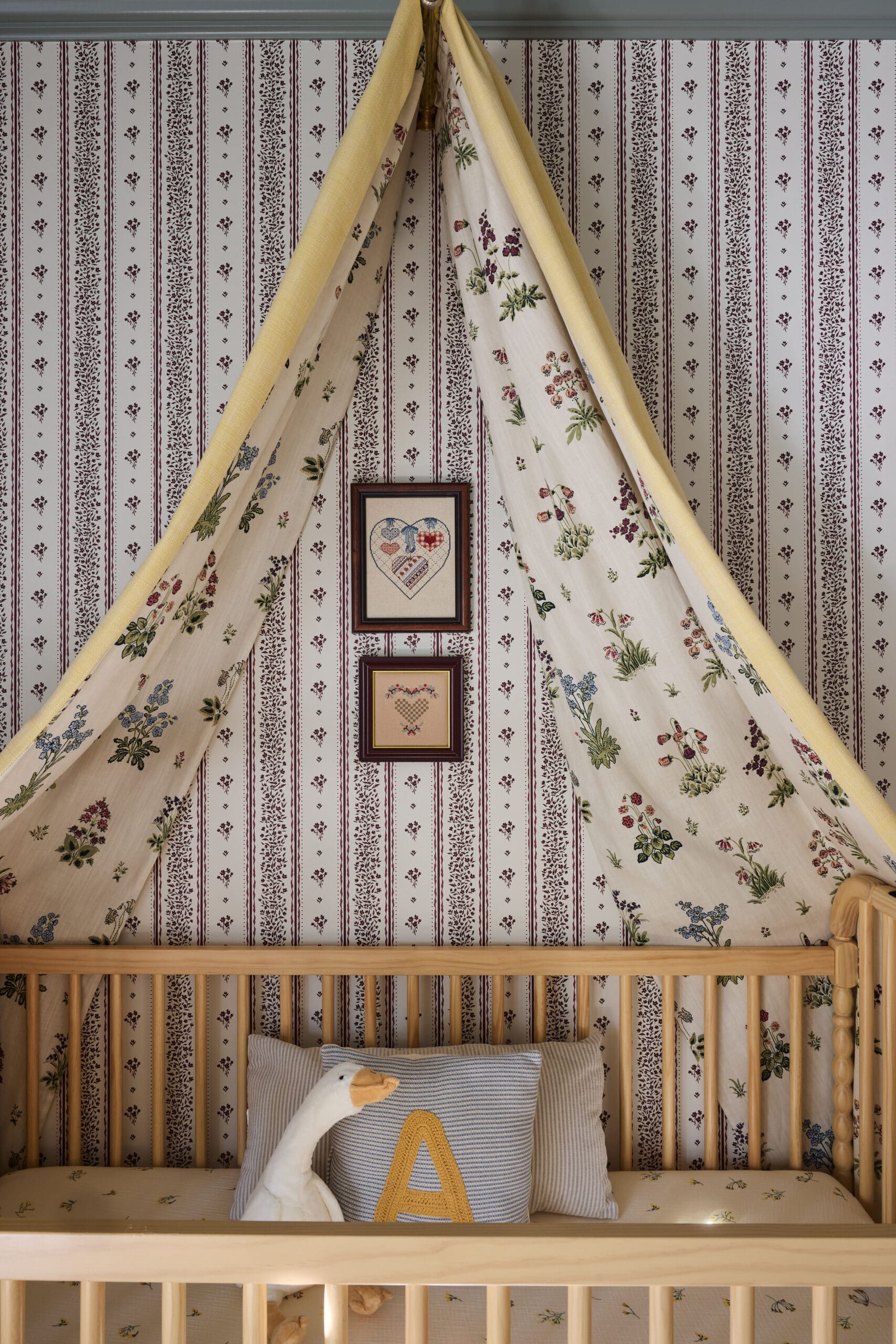 Teal canopy draped over a wooden toddler bed with floral fabric and striped wallpaper in the background.