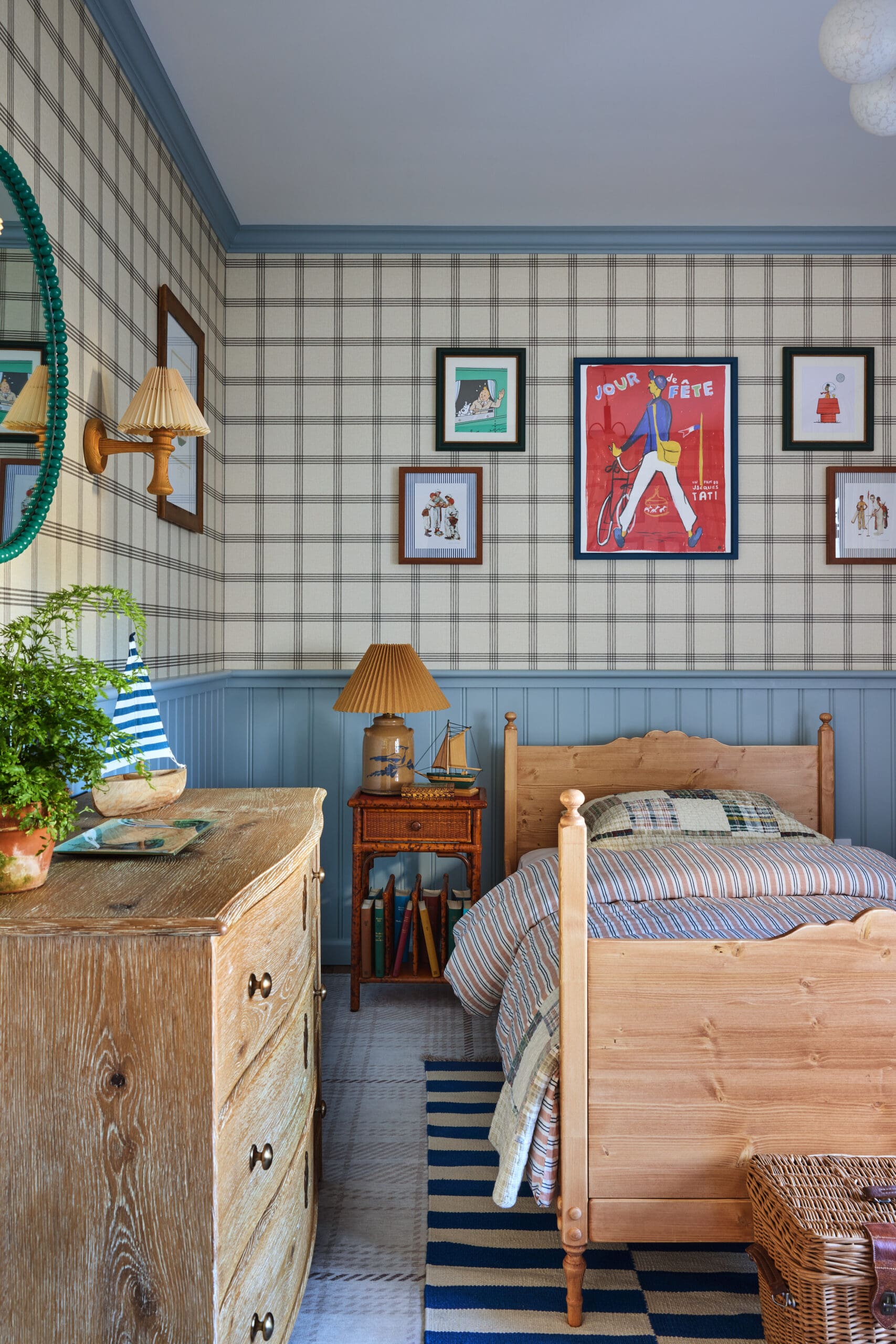 Cozy vintage bedroom with blue wainscot, plaid wallpaper, and a gallery wall of framed art above a wooden dresser and twin bed.