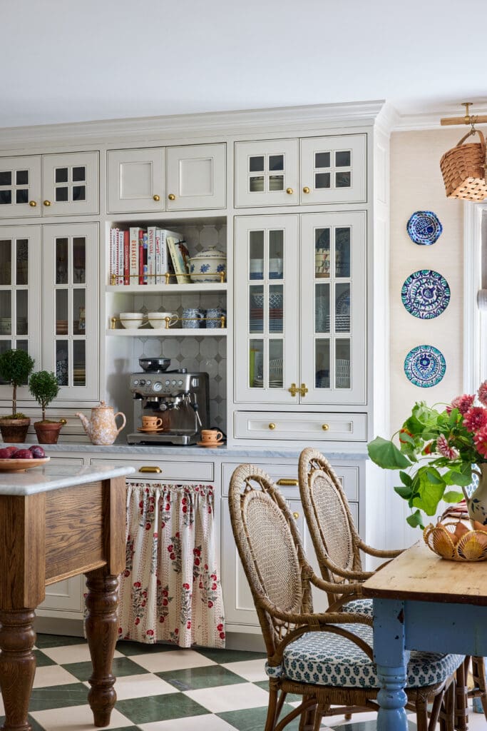 Cream cabinetry with glass doors and brass knobs, a built-in espresso machine on the counter, and blue-and-white dishware on open shelves.