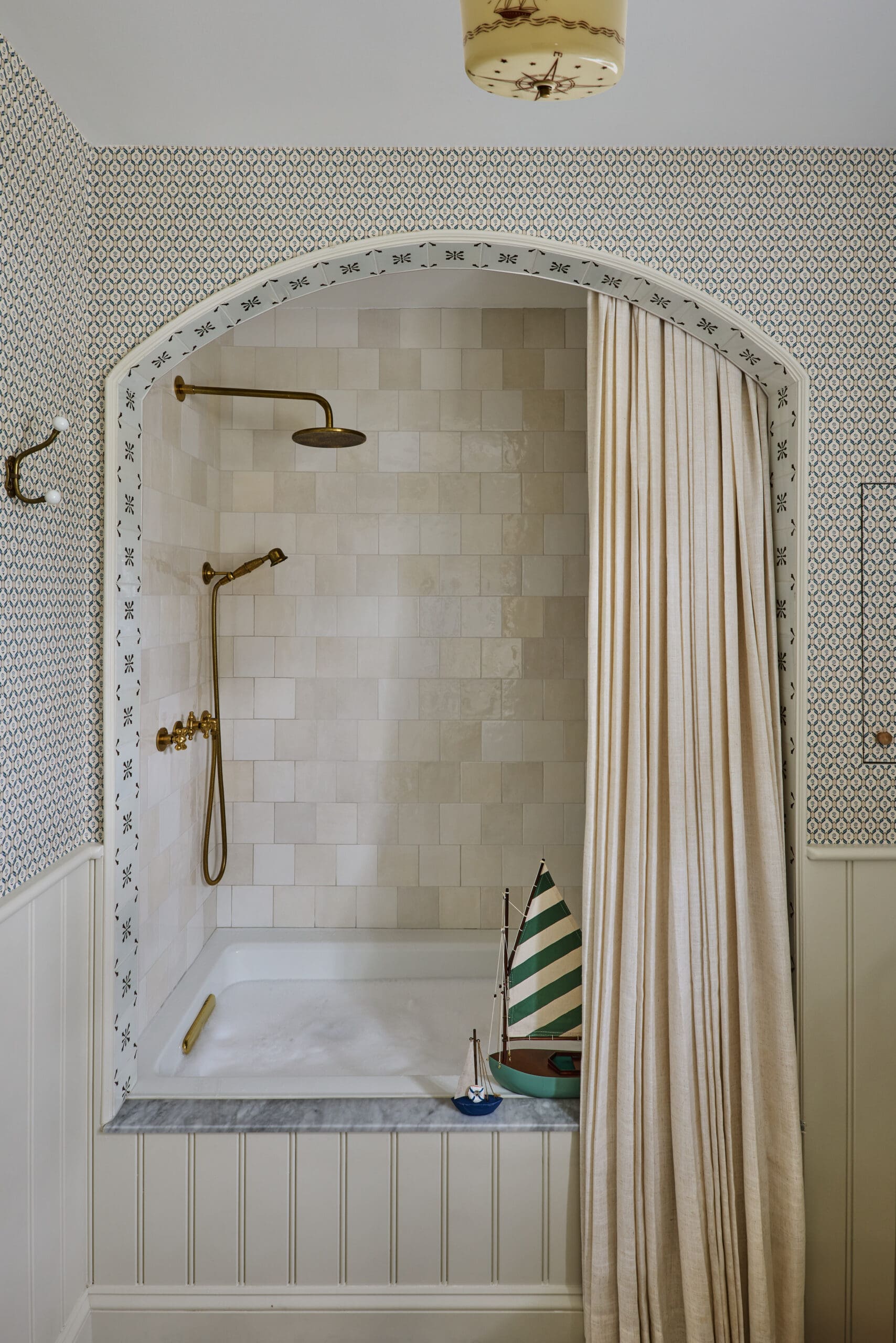 Arched shower alcove with beige tiles, decorative border, and brass fixtures including a rainfall showerhead and handheld wand, curtain to the right.