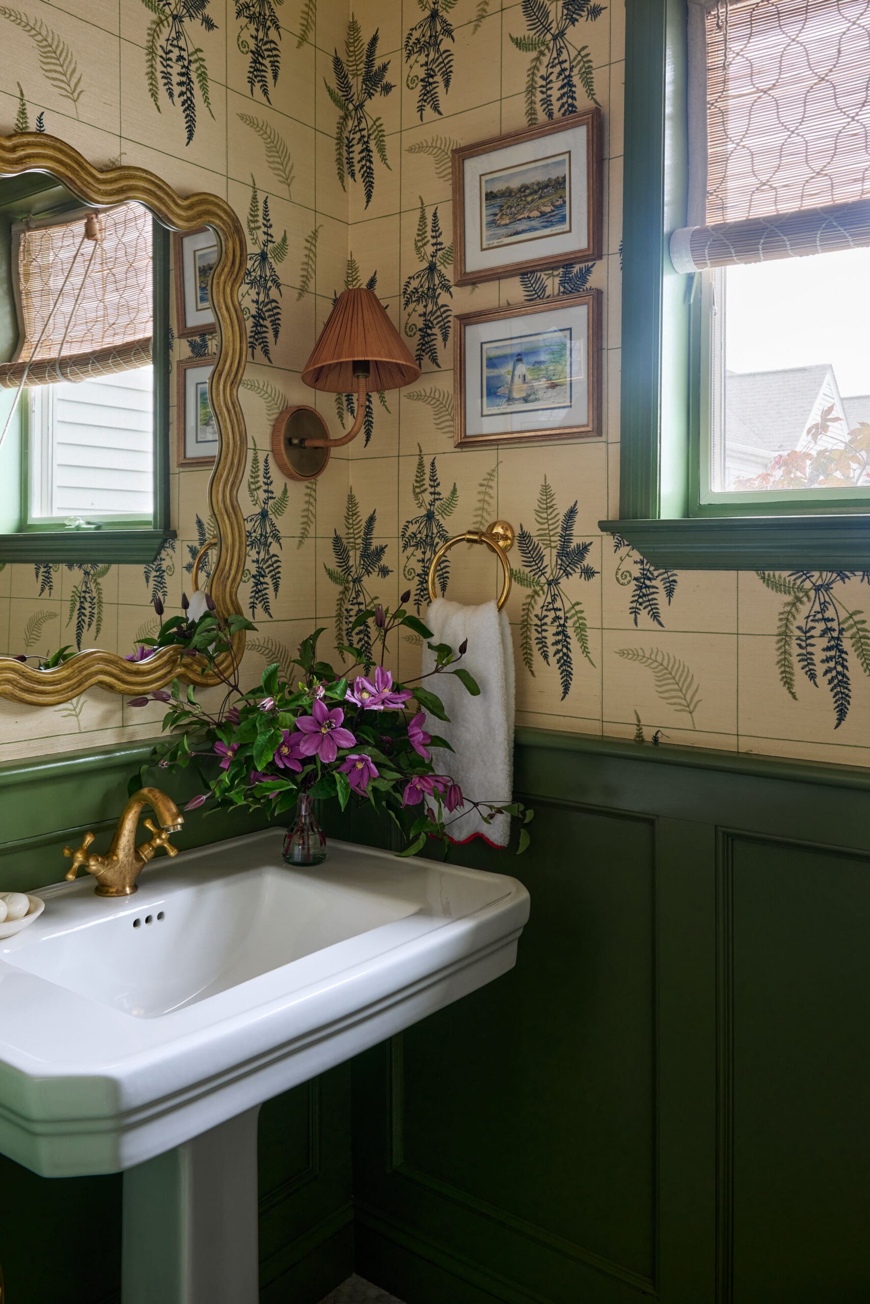 Vintage bathroom with a white pedestal sink, brass faucet, and green paneling beneath fern-pattern wallpaper.