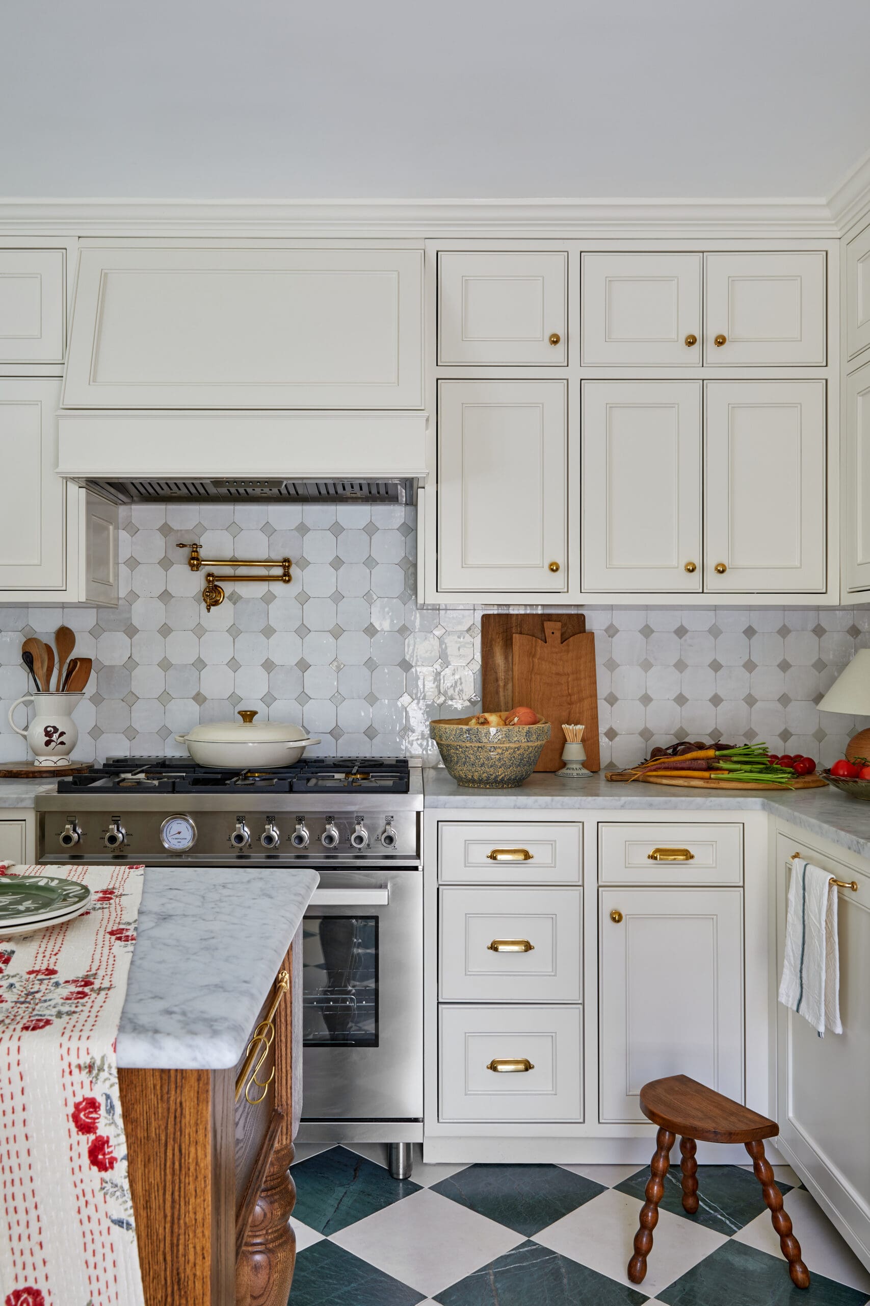White kitchen with cream cabinets, gold knobs, and a stainless stove under a patterned tile backsplash.