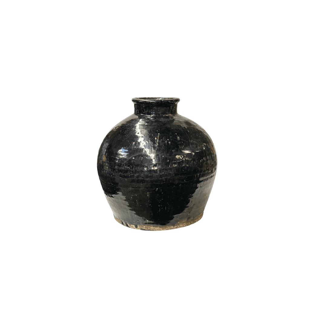 Glossy black ceramic vase with a rounded body and short neck on a rough base, photographed against a black background.
