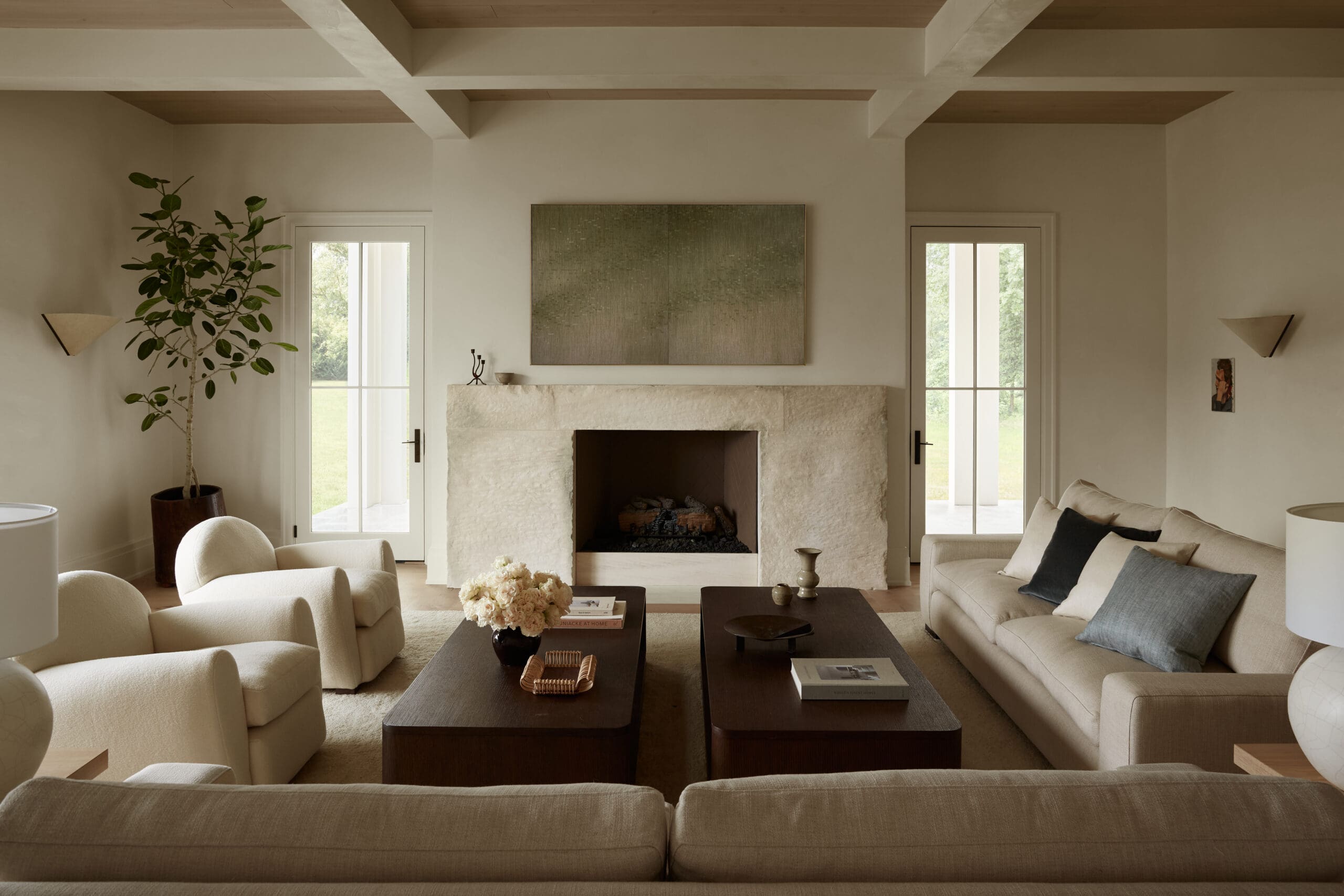 Cozy beige living room with a stone fireplace, abstract art above it, and two glass doors leading outside.