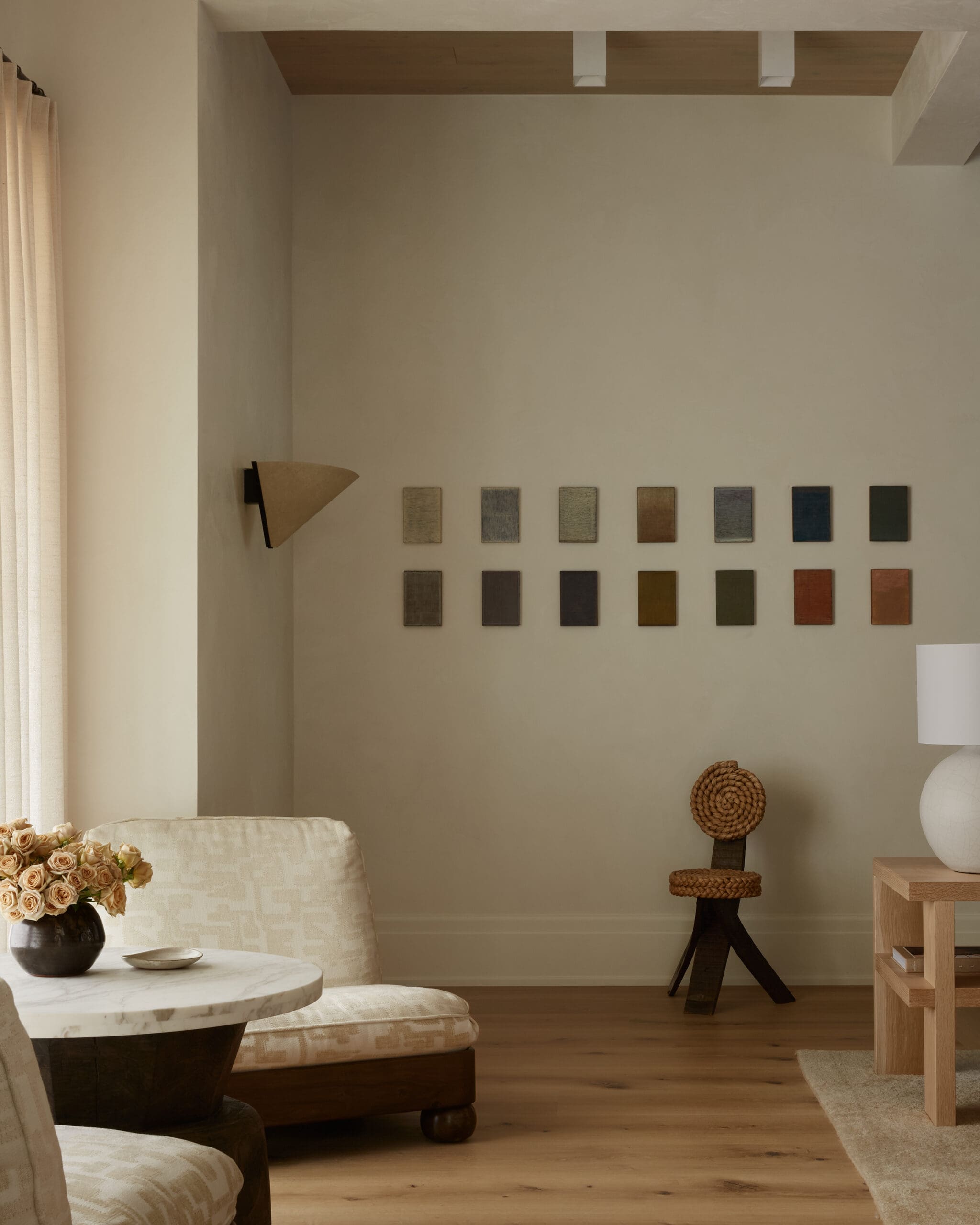 Living room corner with beige walls, a row of paint swatches on the wall, and a bouquet on a marble coffee table.