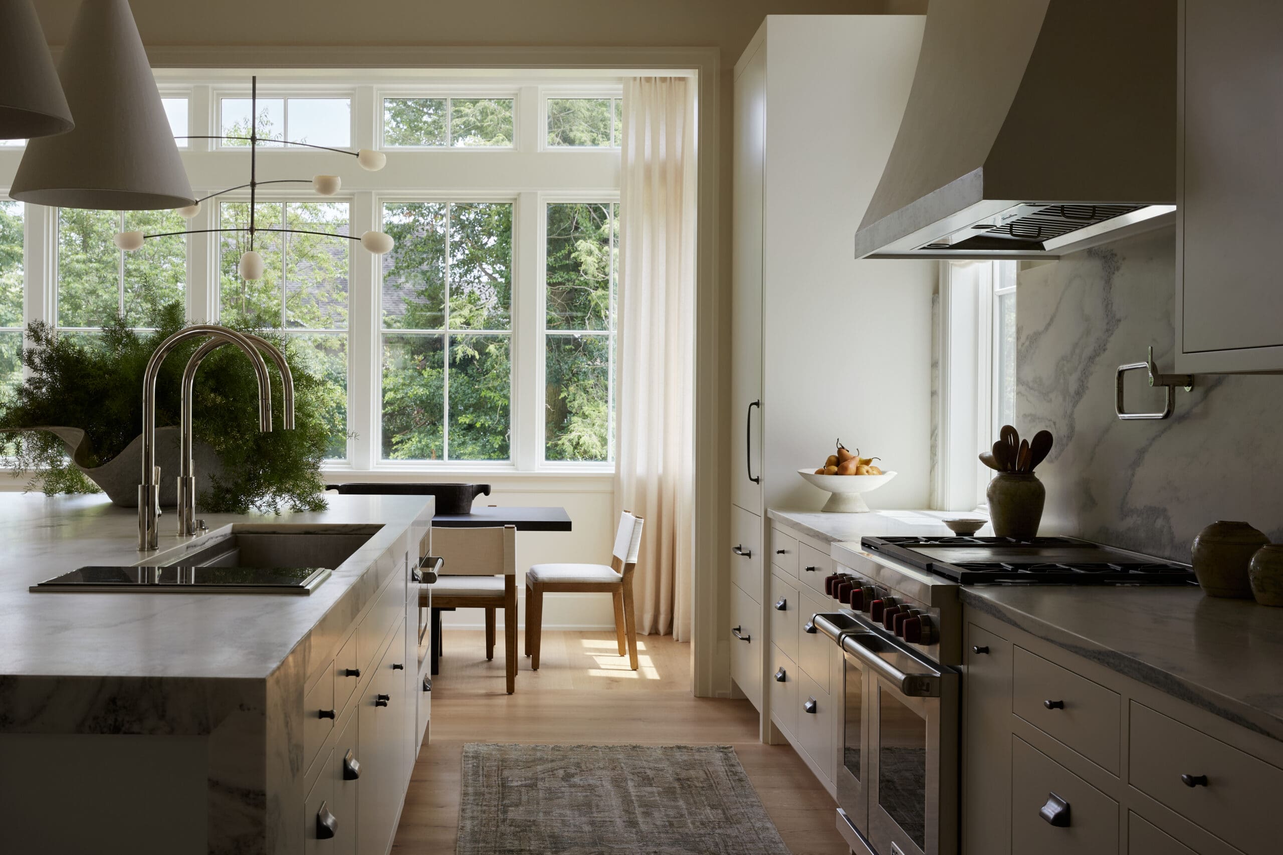 Bright, modern kitchen with marble countertops, an island sink, and large windows looking out on trees and greenery.