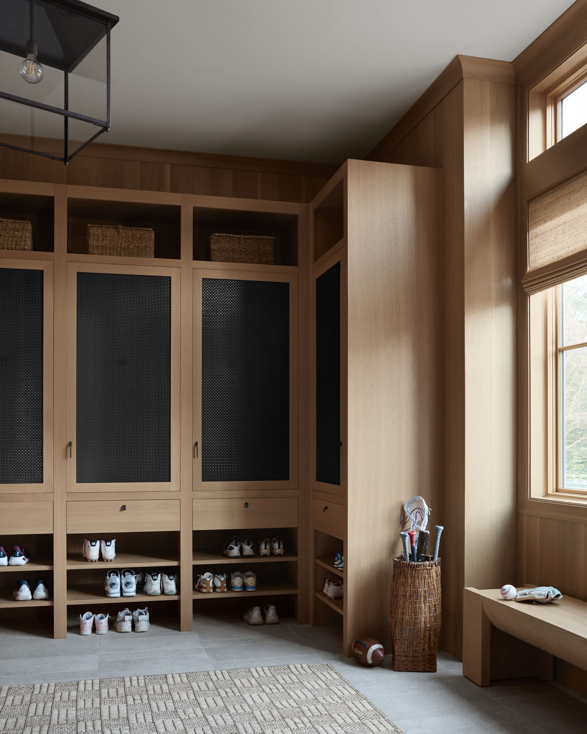 Wooden built-in storage with cubbies and mesh-front doors, used to store shoes and baskets in a bright room with a window to the right.