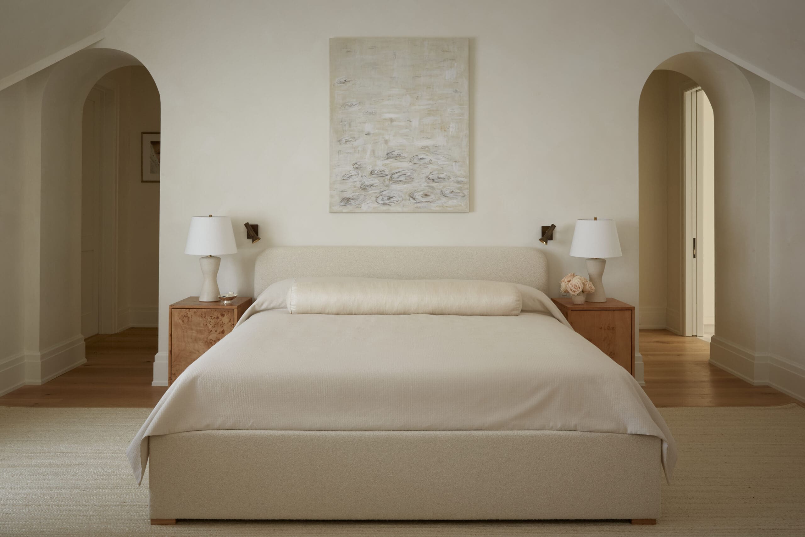 Neutral-toned bedroom with a large bed, two wooden nightstands, lamps, and an abstract painting above the headboard in soft beige hues.