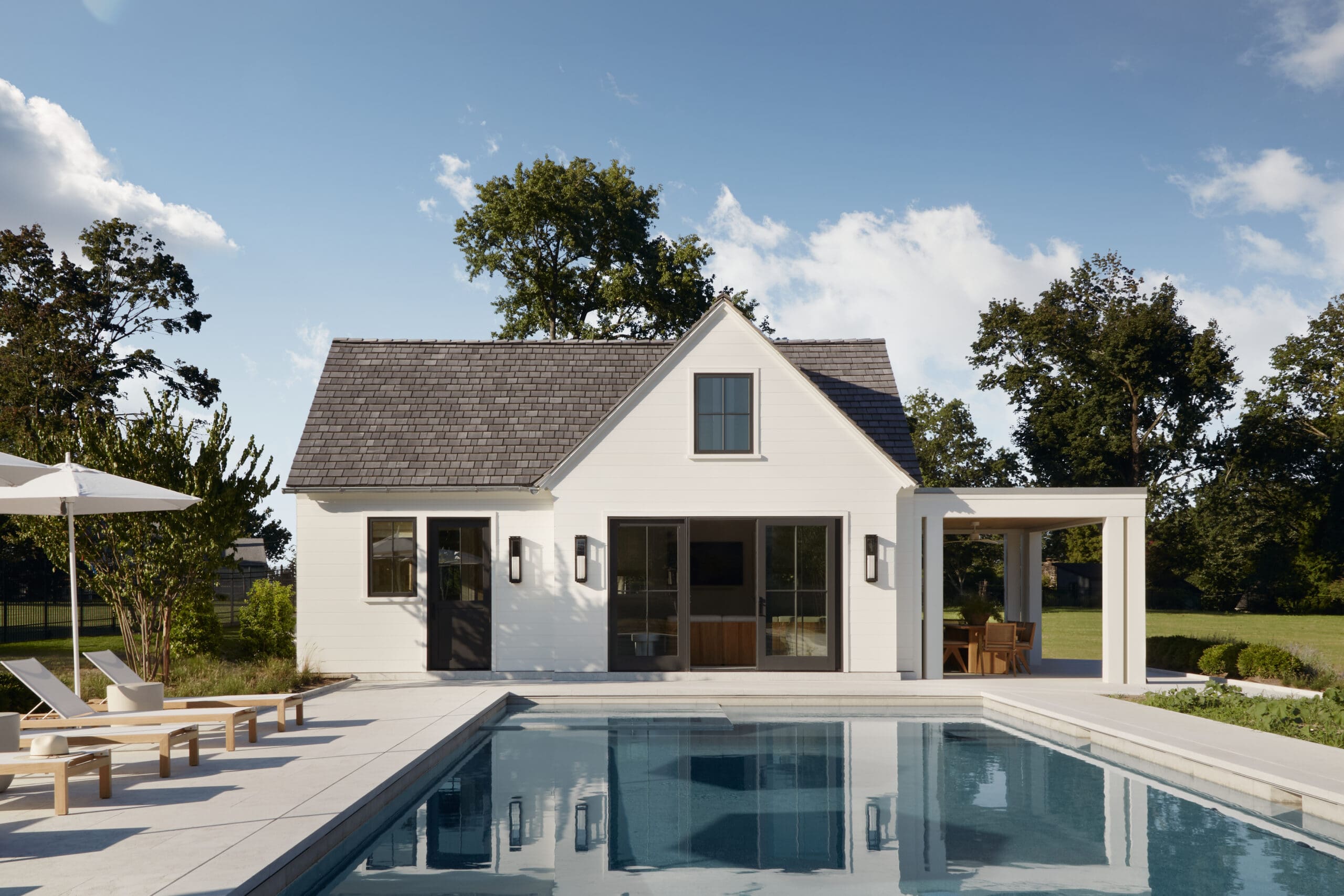 Modern white house with a triangular roof, large glass doors, and a rectangular pool in the foreground.