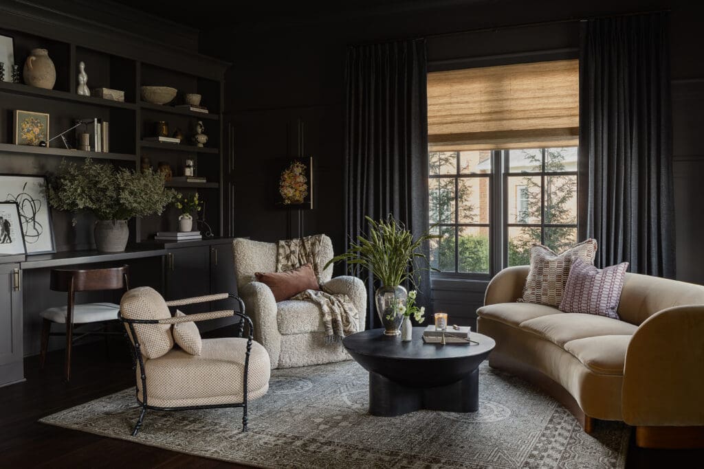 Cozy living room with dark walls, built‑in bookshelves, and a large window with woven shades and dark curtains.