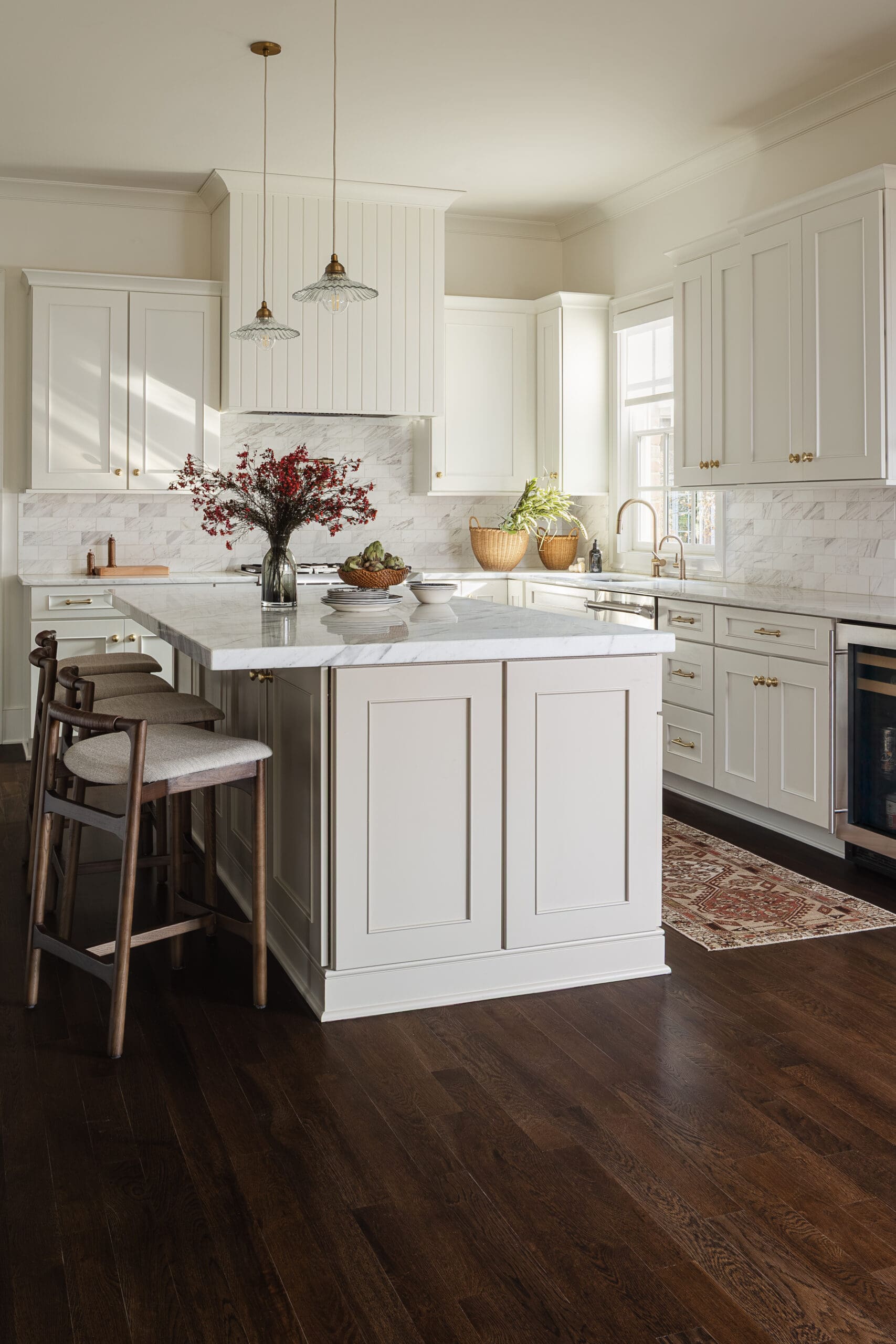 Bright white kitchen with marble-topped island, brass hardware, and two pendant lights above the counter.