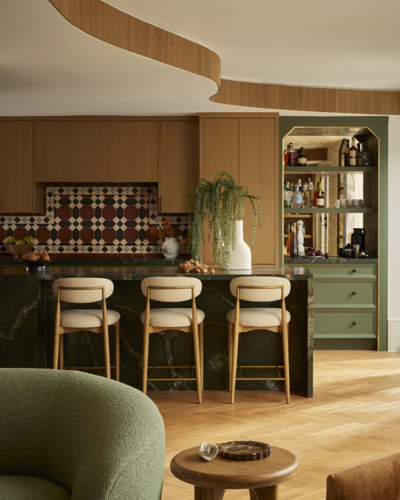 Modern kitchen with warm wood cabinets, a patterned tile backsplash, and a dark marble island with beige bar stools at the counter edge.