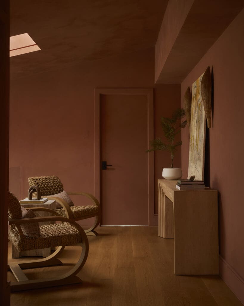 Brown-toned living room corner with two woven wicker chairs, a wooden console, a potted plant, and decorative wall art leaning against the wall.