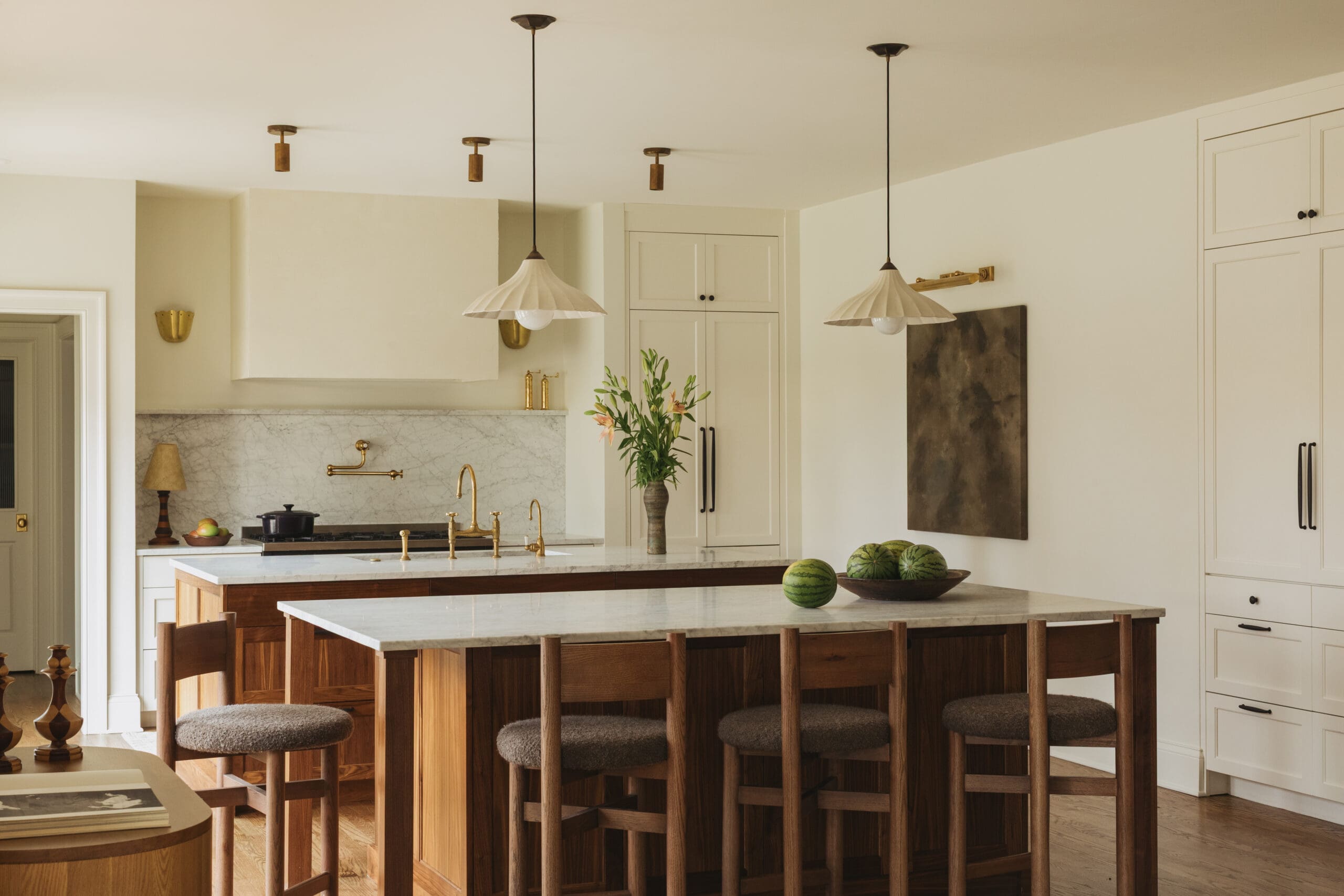 Kitchen with marble countertops and white cabinets, wooden island and four bar stools; bowl of watermelons on the island.