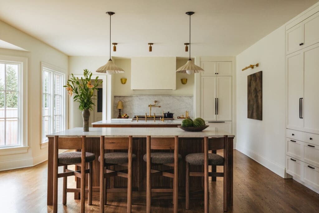 Bright, airy kitchen with white cabinets, marble backsplash, and a large wooden island with stools beneath pendant lights.