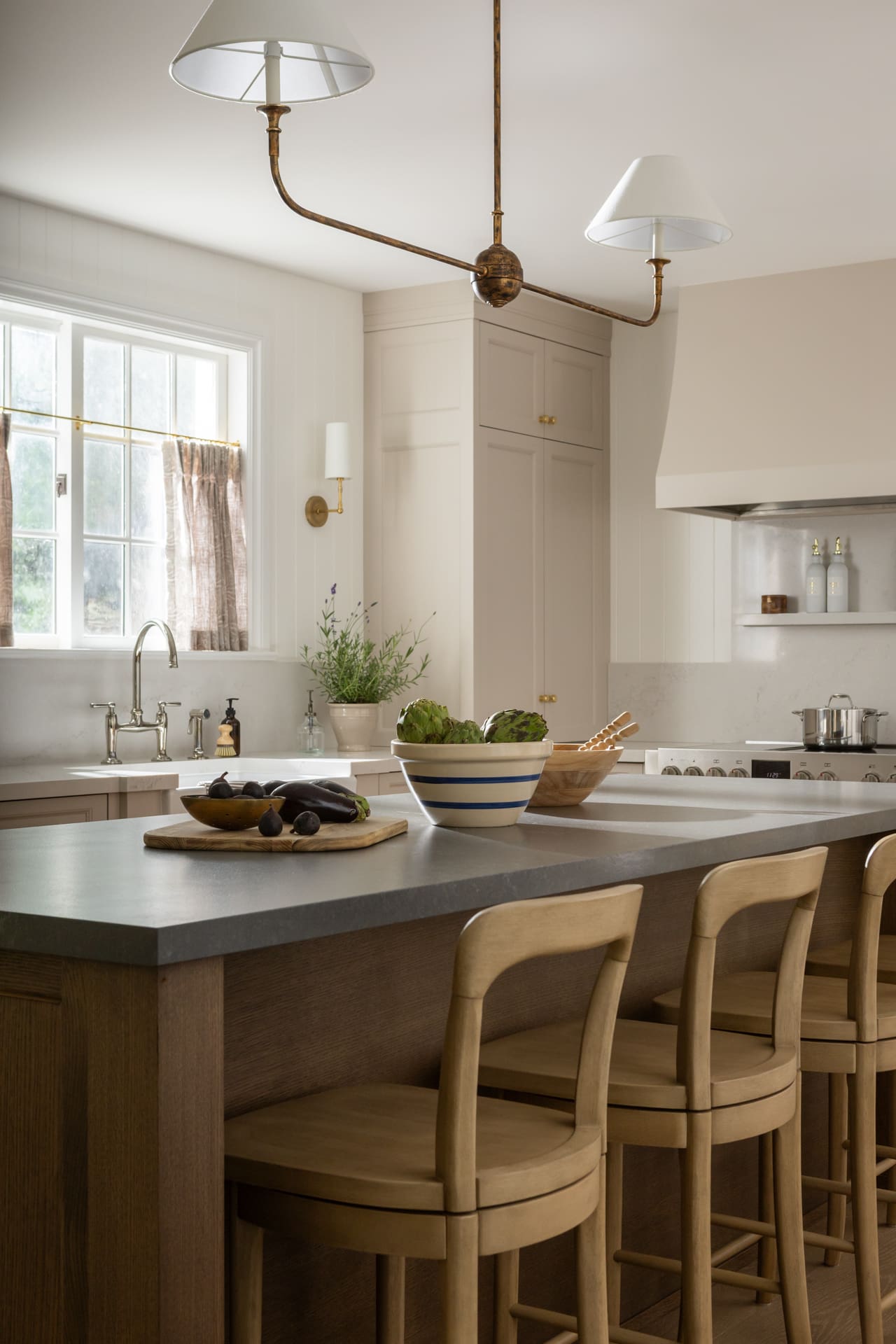 Modern kitchen with a large wooden island, light wood stools, and a brass vintage-style chandelier above the island.