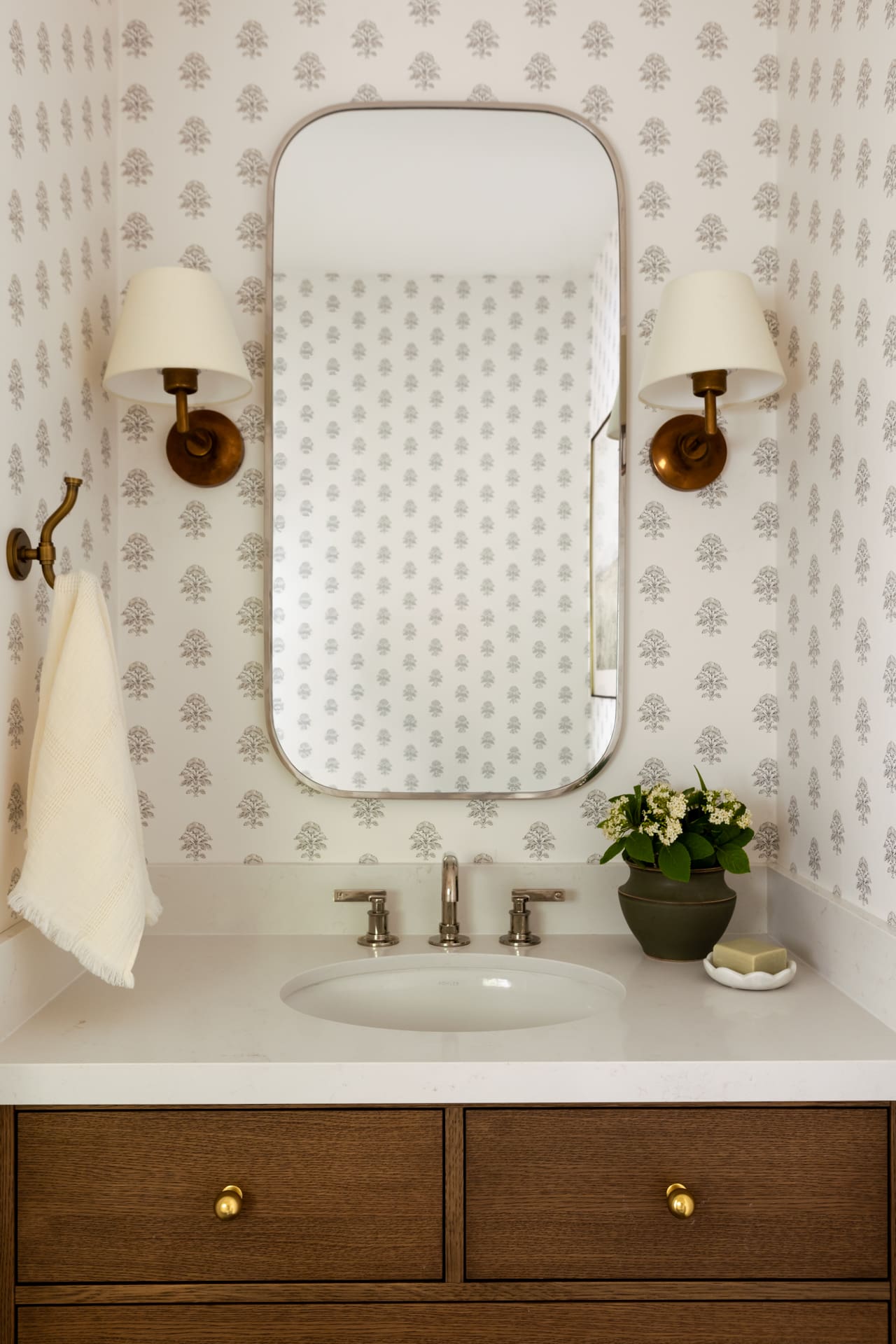 Wood vanity with a white countertop, oval sink, brass pulls, and two brass wall sconces in a vintage bathroom.