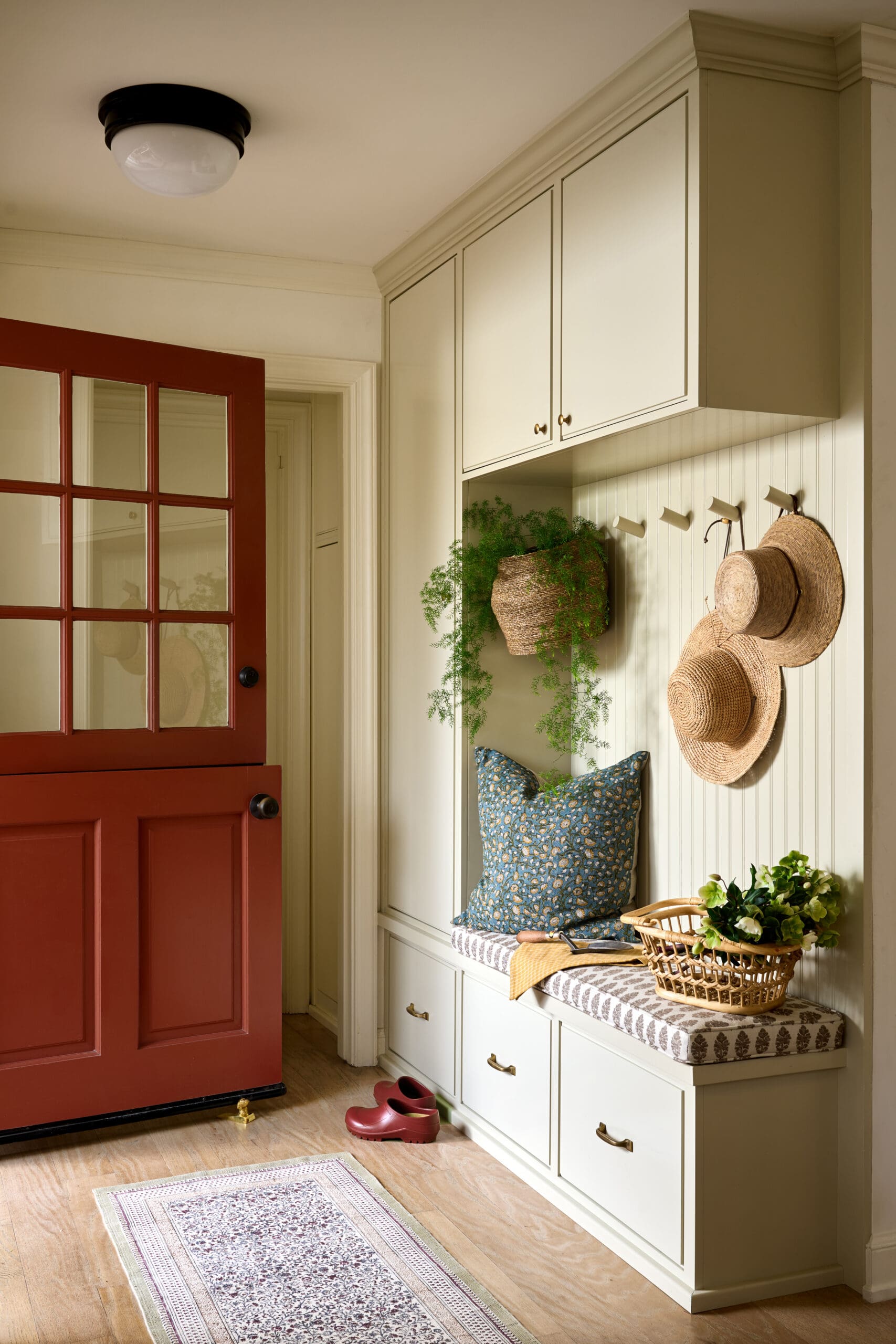 Entryway mudroom with cream built-in cabinets, a red paneled door, and a bench area with cushions and a wicker basket.