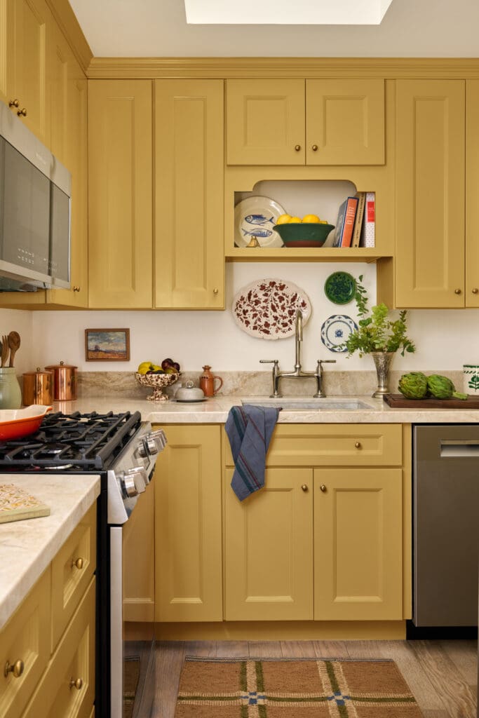 Yellow kitchen with open shelf displaying a fruit bowl, plates, and cookbooks above a sink area