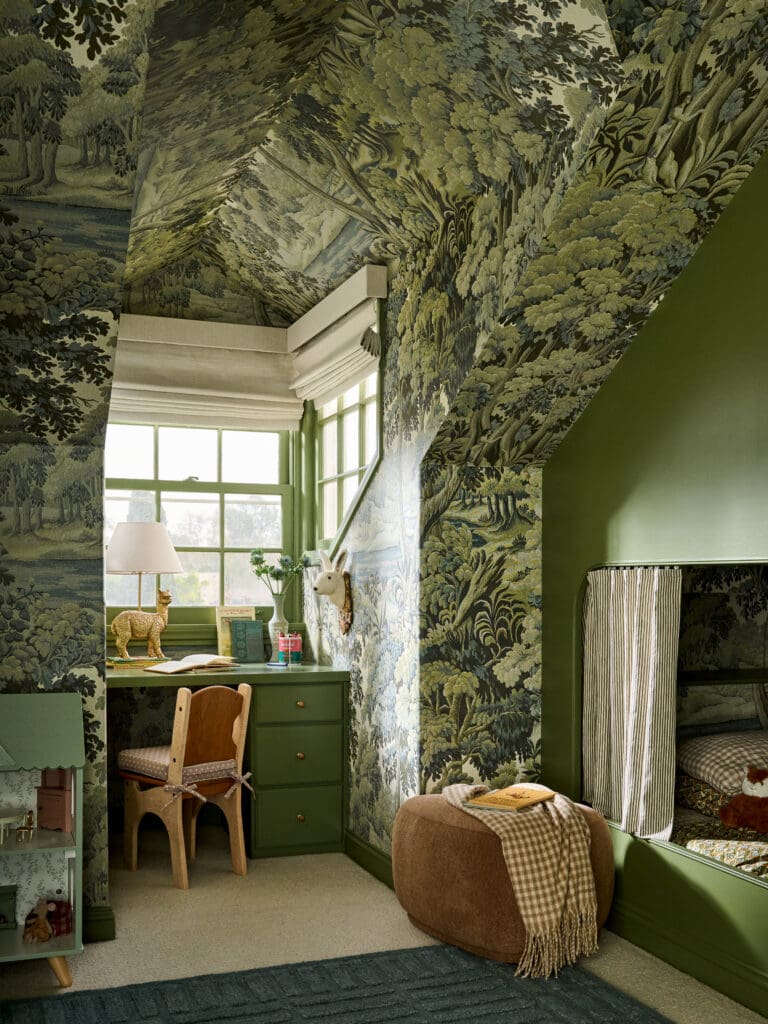 Green toile wallpapered study nook with a desk, chair, lamp, and a deer figurine by a window.
