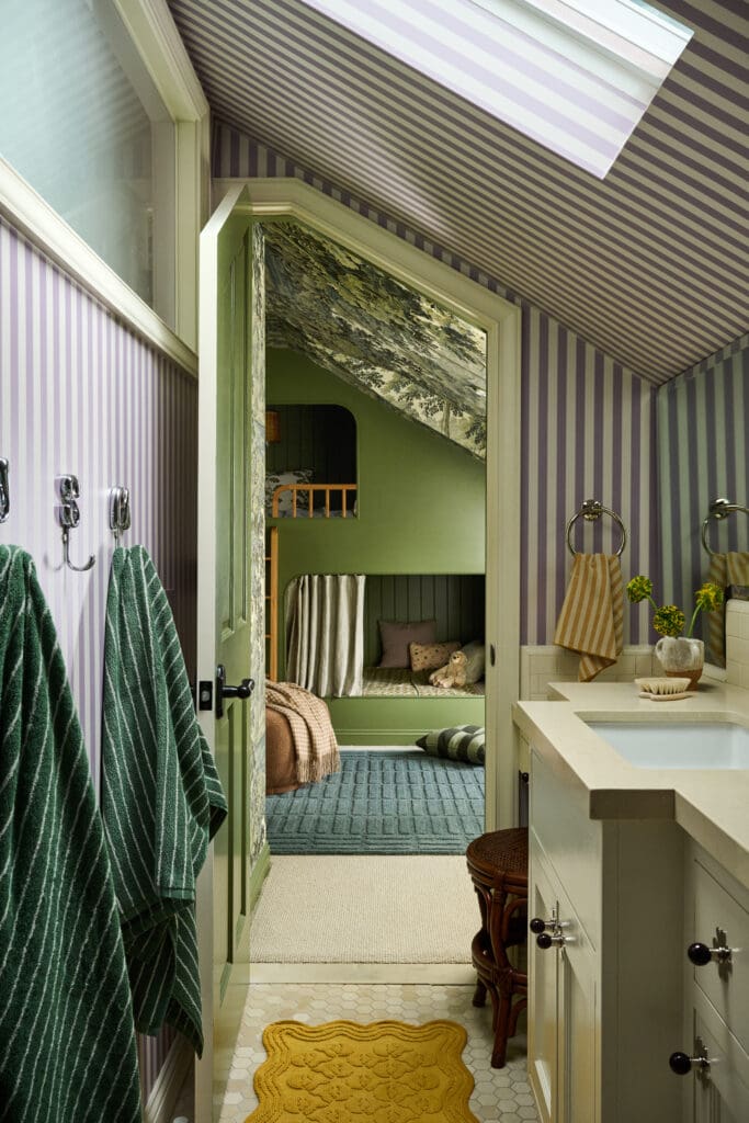 Bathroom hallway with lavender and white striped walls, open green doorway revealing a green bedroom with a bunk and cozy bedding.