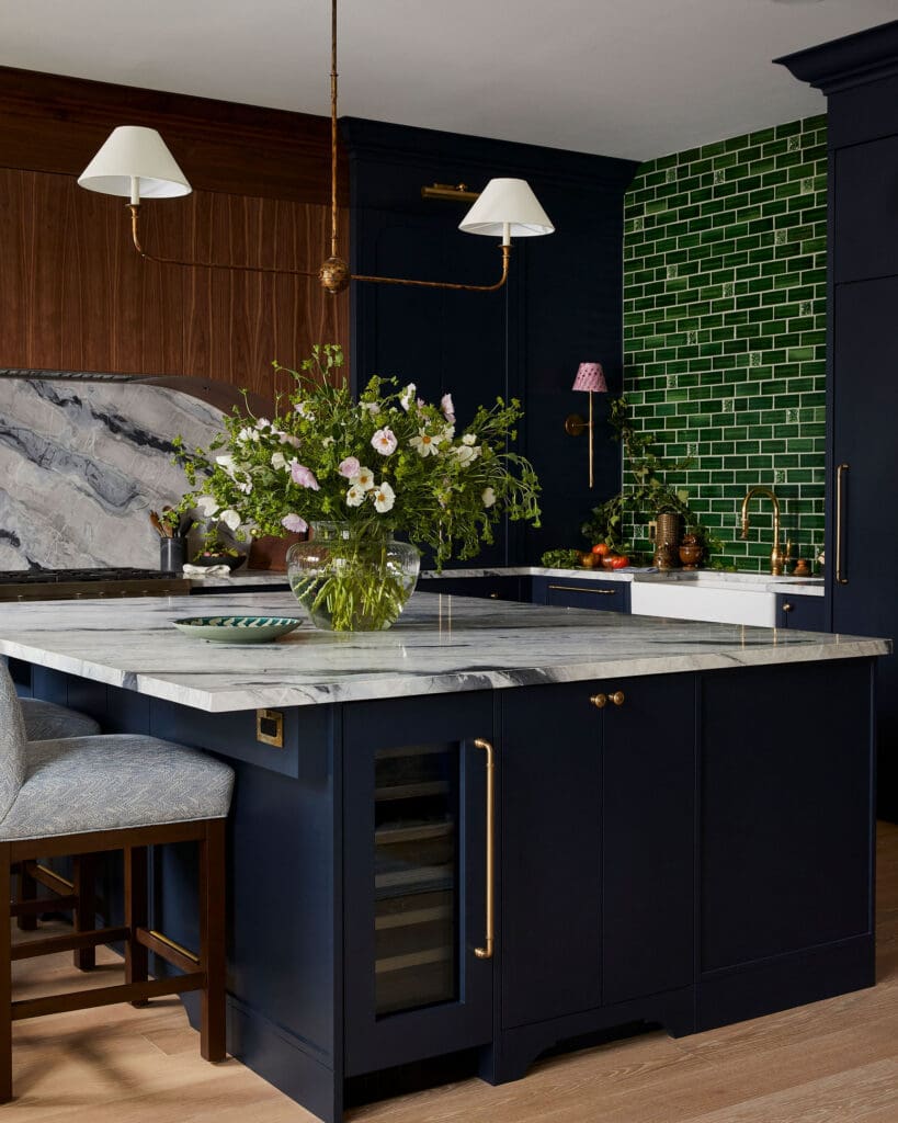 Navy kitchen with marble island, brass accents, and a large glass vase of wildflowers.