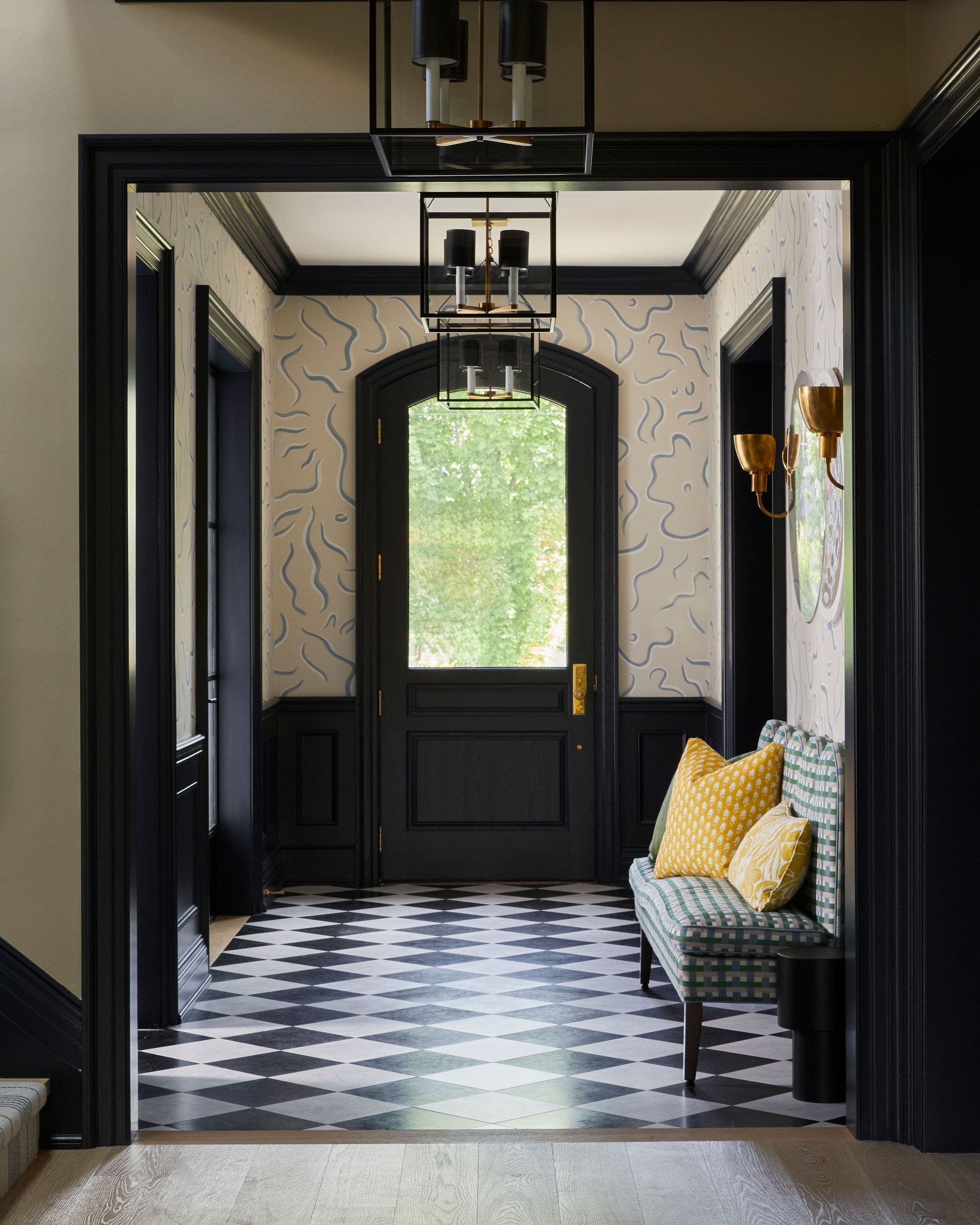 Entry hallway with black trim, checkered black-and-white floor, and a green striped bench with yellow pillows.