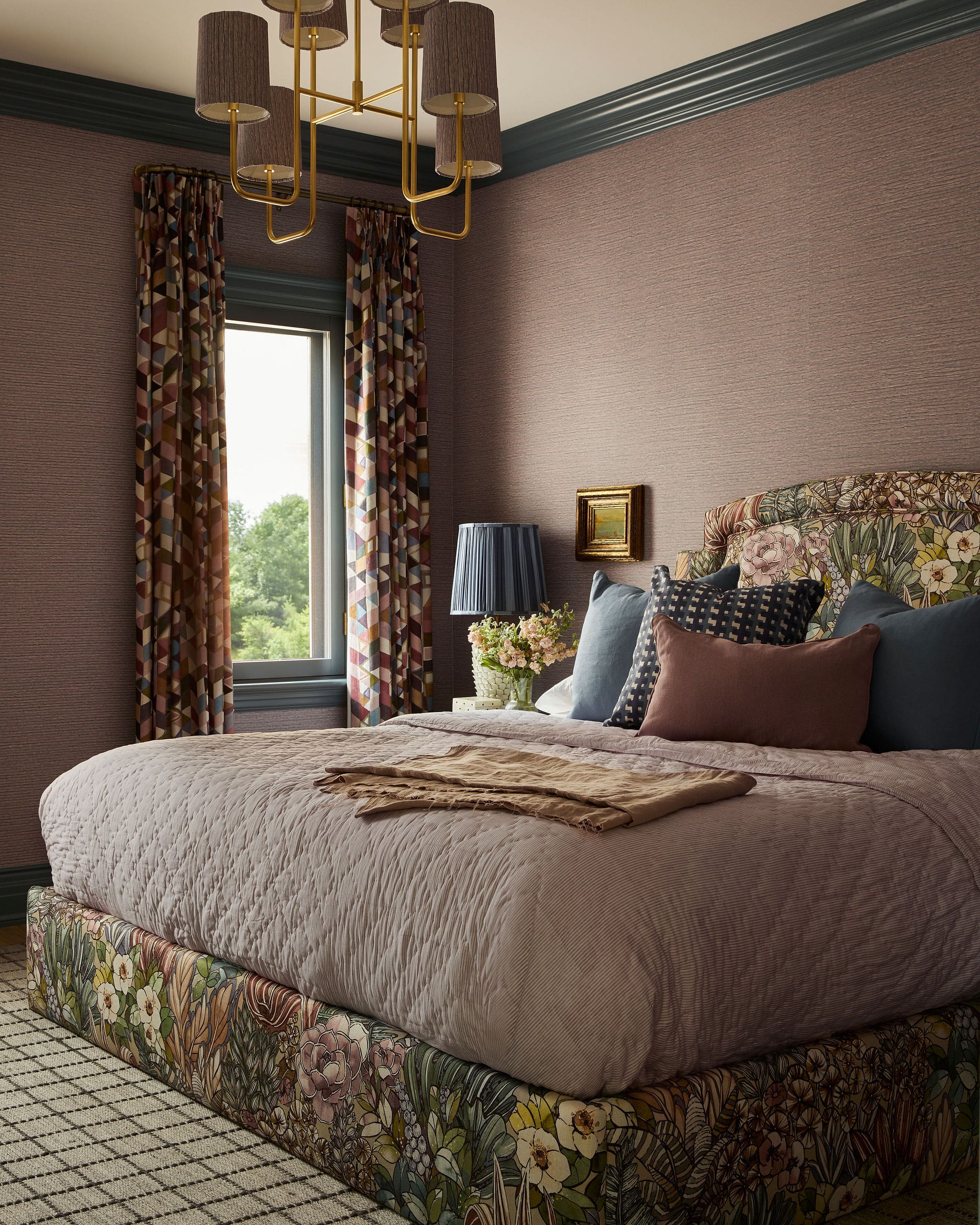Luxurious bedroom with mauve walls, gold chandelier, patterned curtains, and a floral upholstered bed base.