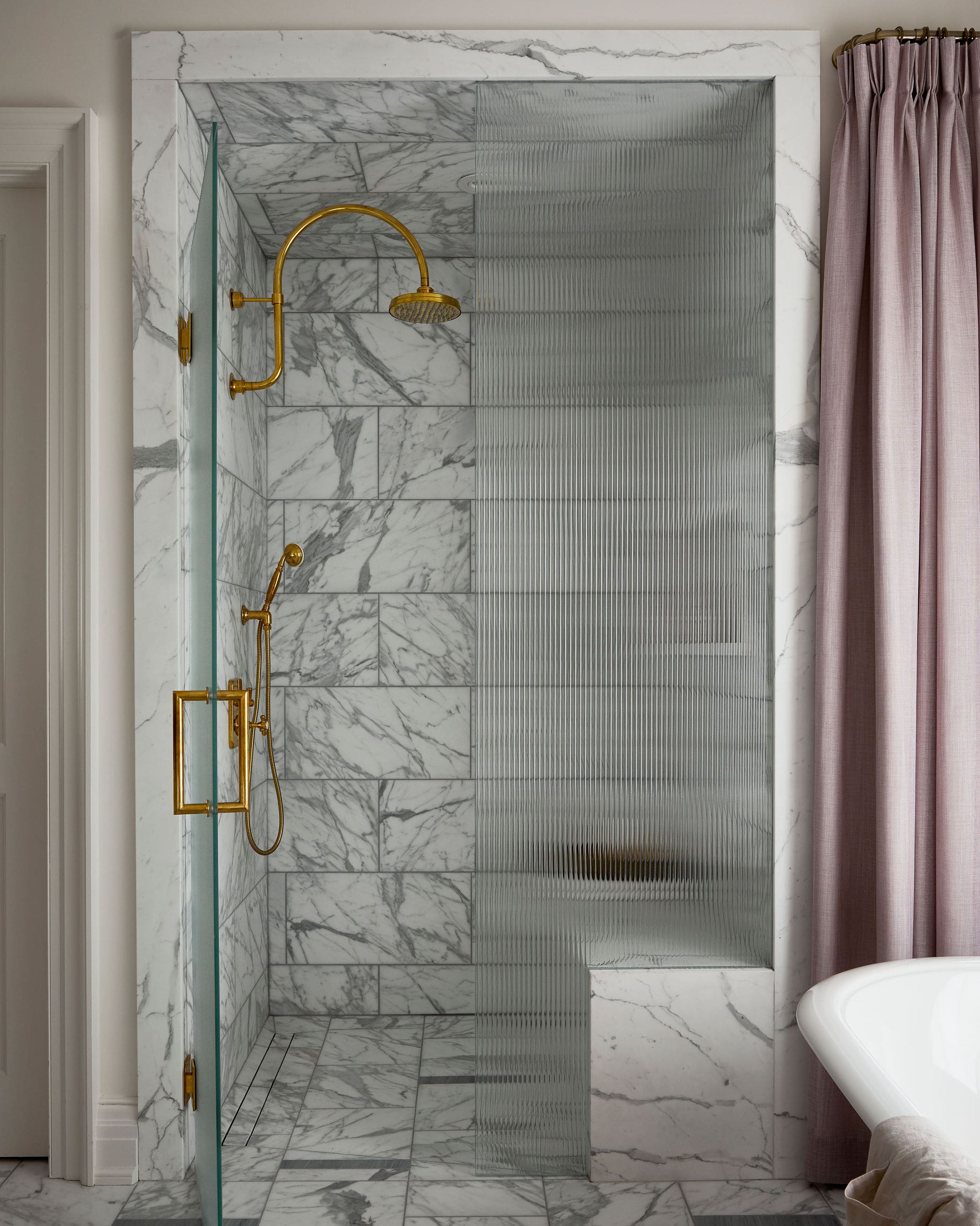 Luxurious marble shower with gold fixtures and a textured glass screen, pink curtain to the side.