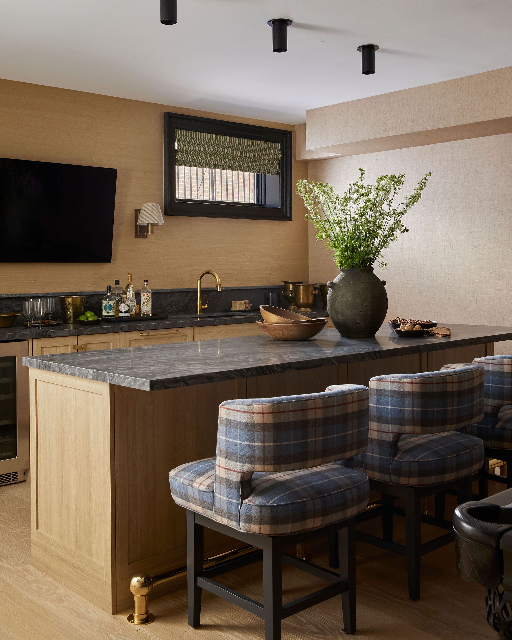 Modern kitchen bar with a marble countertop, beige walls, and plaid-upholstered stools around a black-framed island.