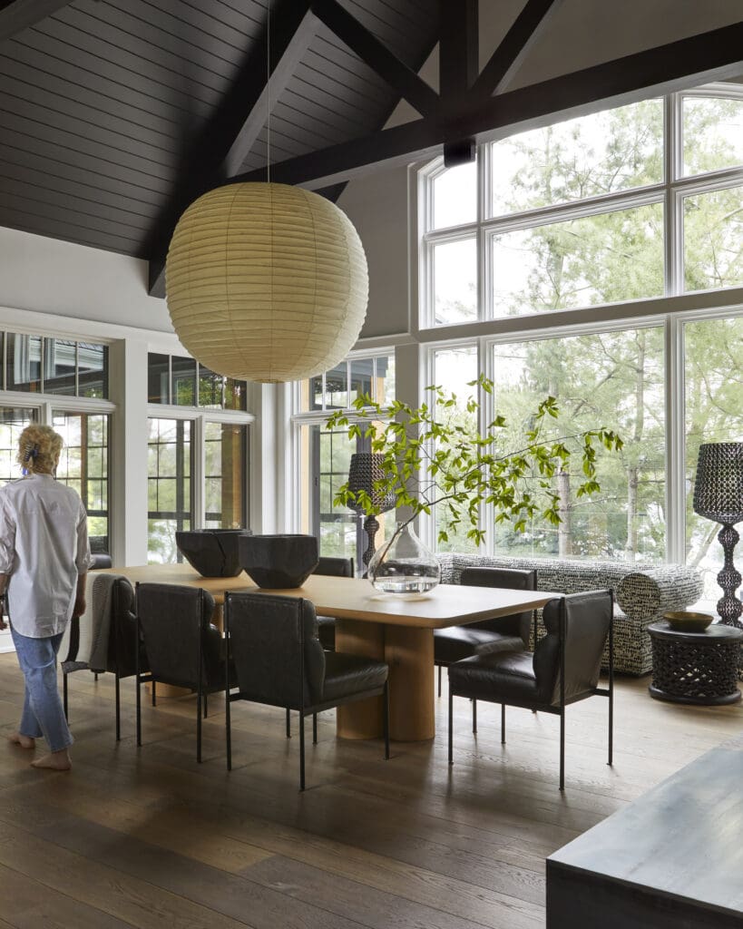 Elegant dining area with a large round paper lantern hanging from a dark wooden beam ceiling and tall windows letting in natural light.