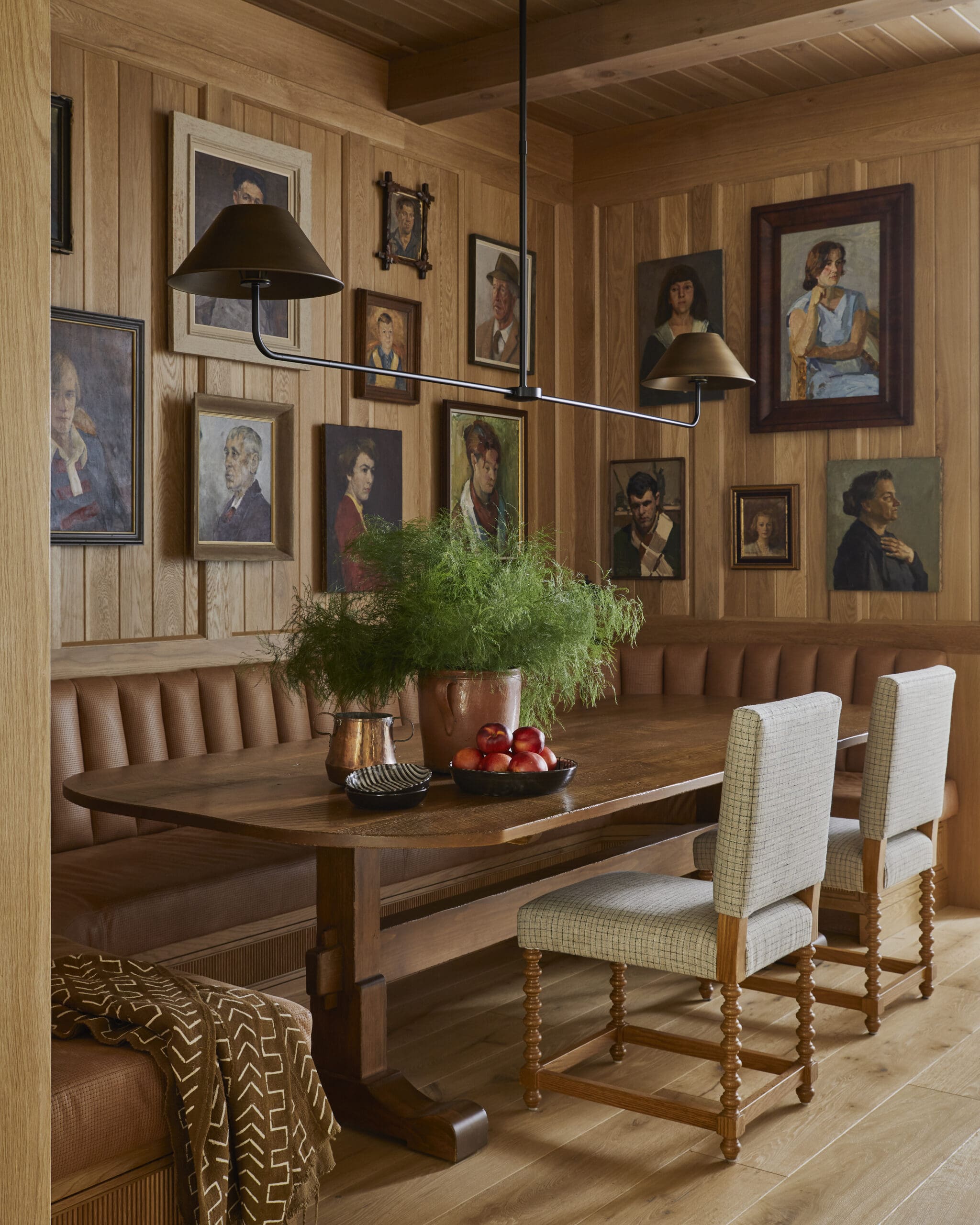 Wood-paneled dining nook with framed portraits on the walls, a long wooden table, and hanging lamps above the bench seating.