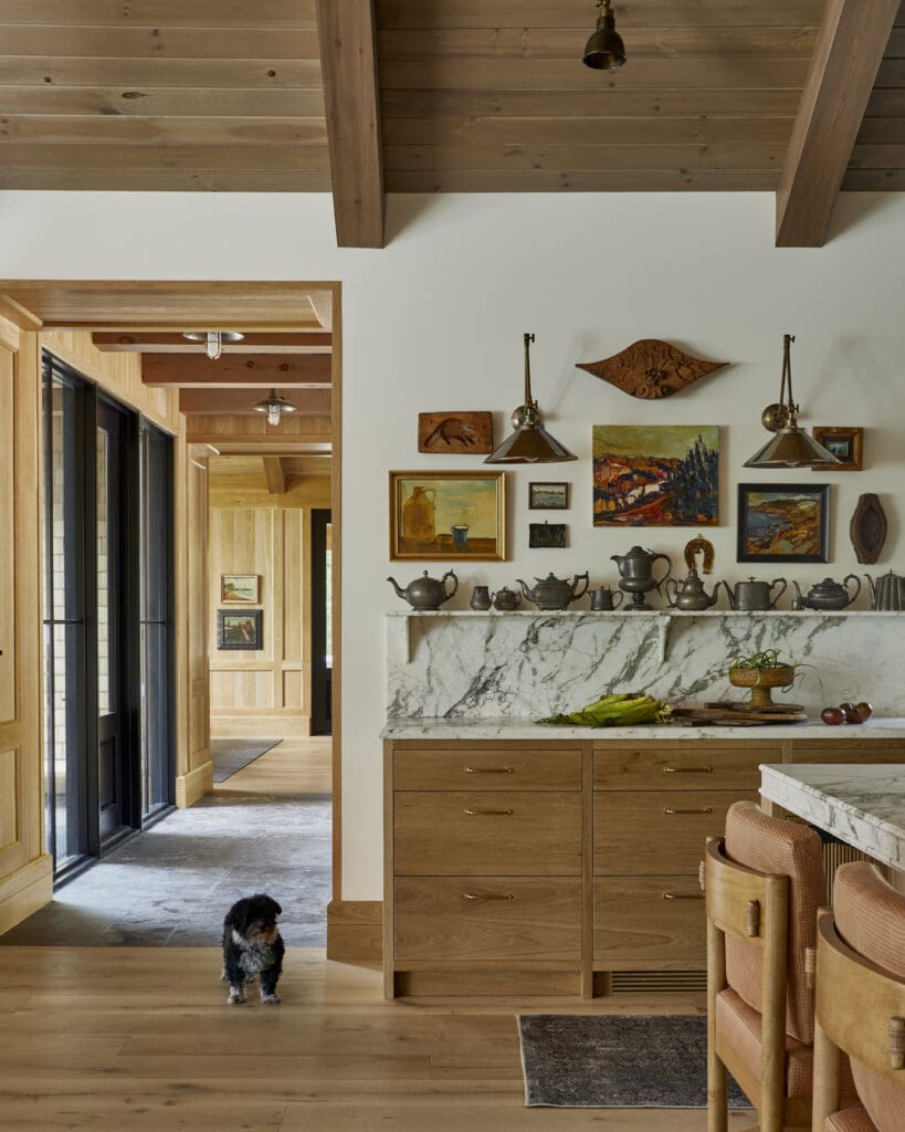 Wooded ceiling beams and a gallery wall with paintings and teapots, a marble counter, and a small dog in the foreground