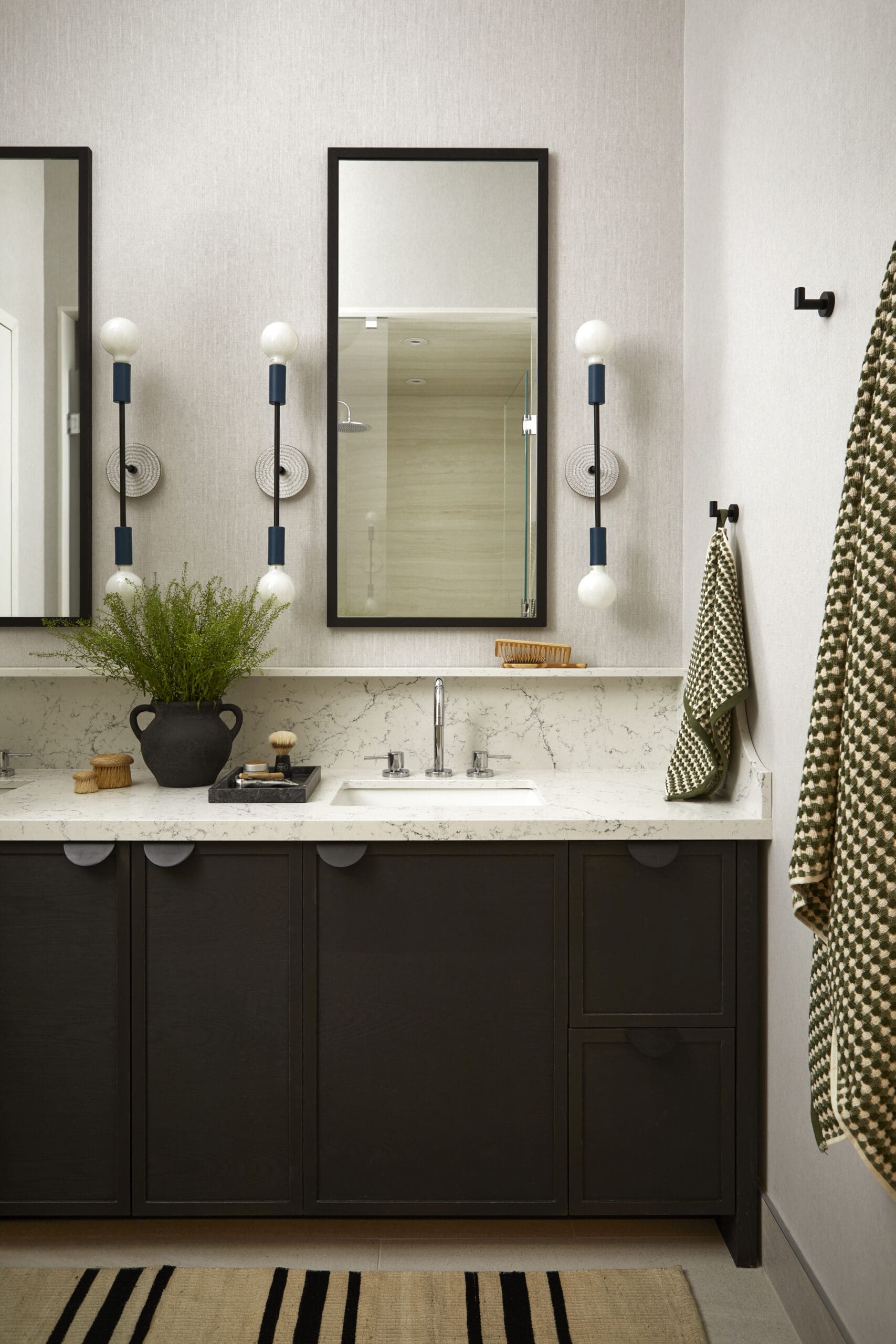 Modern bathroom vanity with a marble countertop, dark cabinets, and two framed mirrors flanked by blue-trost sconces. A potted plant sits on the counter as a decorative touch.