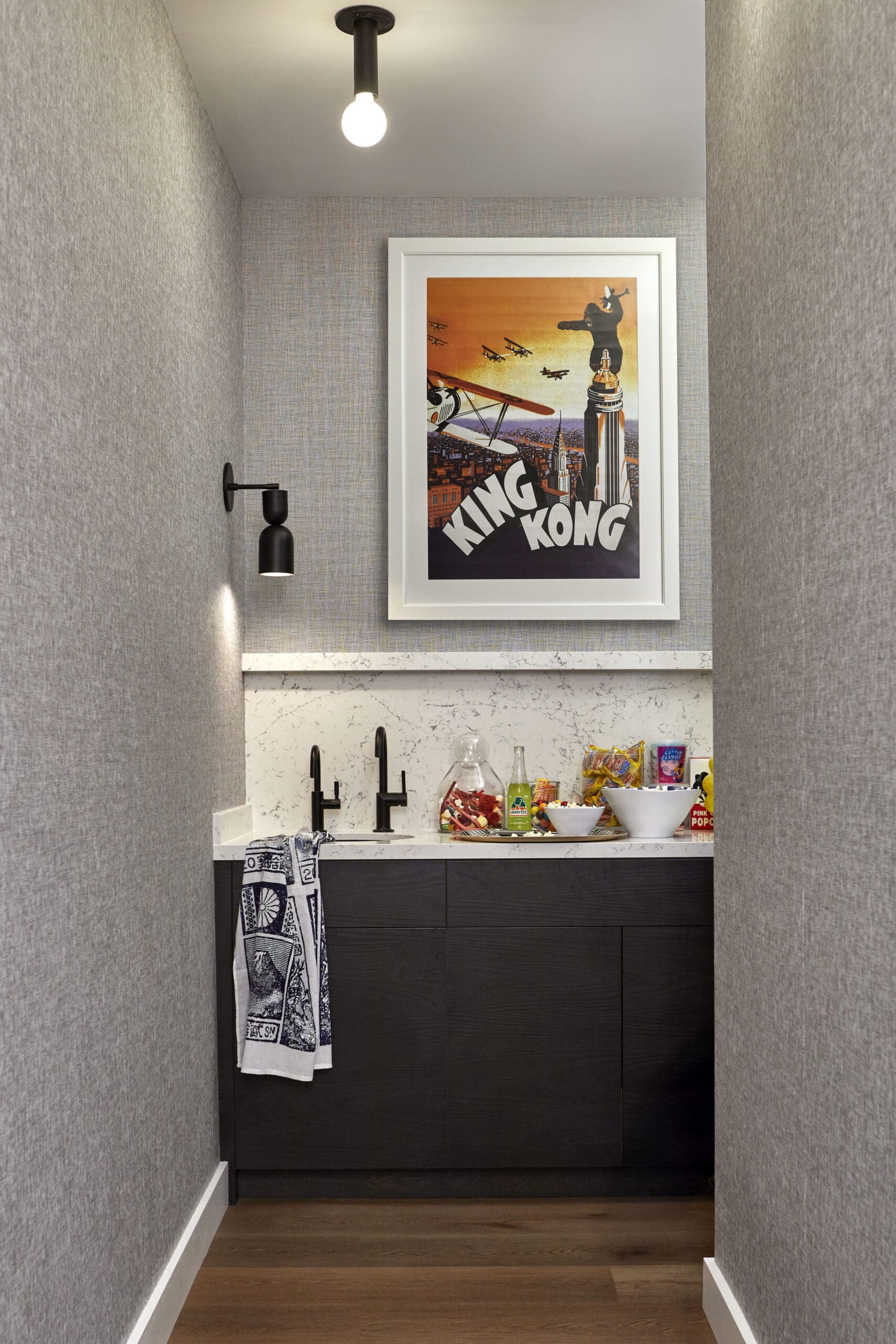 Framed King Kong poster on textured gray walls above a marble counter in a narrow kitchenette nook.