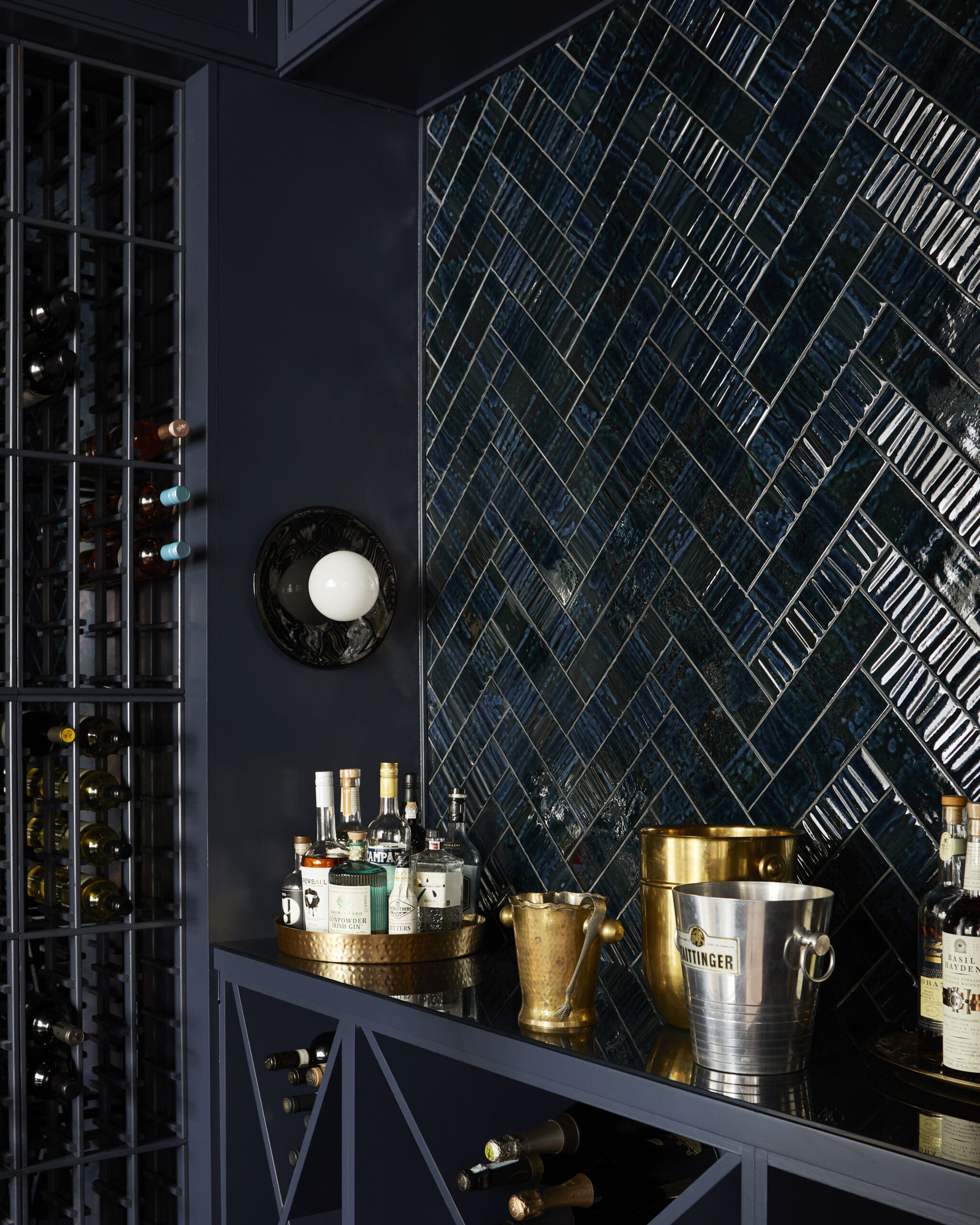 Wine bottles on dark blue shelves beside a blue tiled wall and bar counter.
